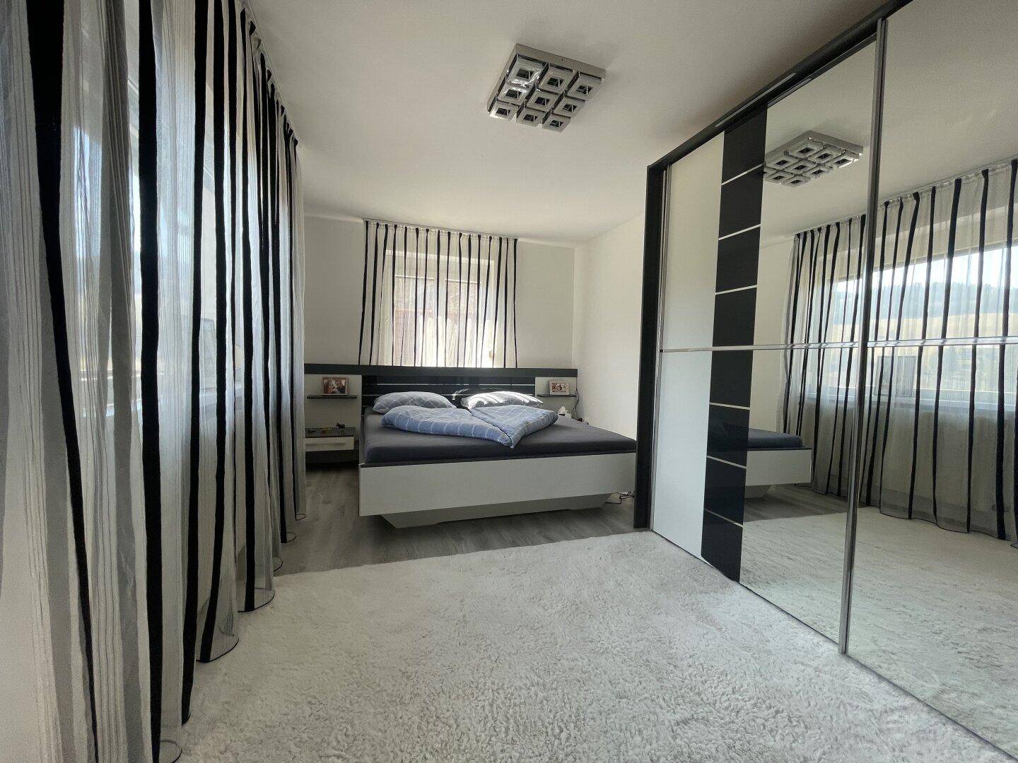 Modernes Schlafzimmer mit Doppelbett, Spiegelschränken und Teppichboden.