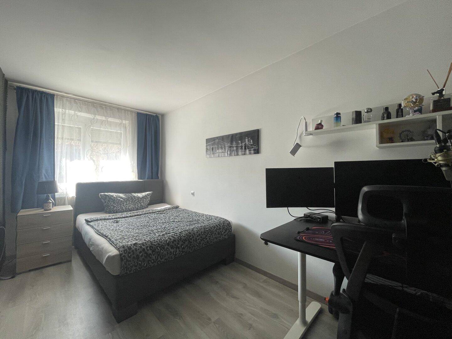 Helles Zimmer mit Bett, Schreibtisch und Computermonitoren, ideal als Schlaf- oder Arbeitszimmer.