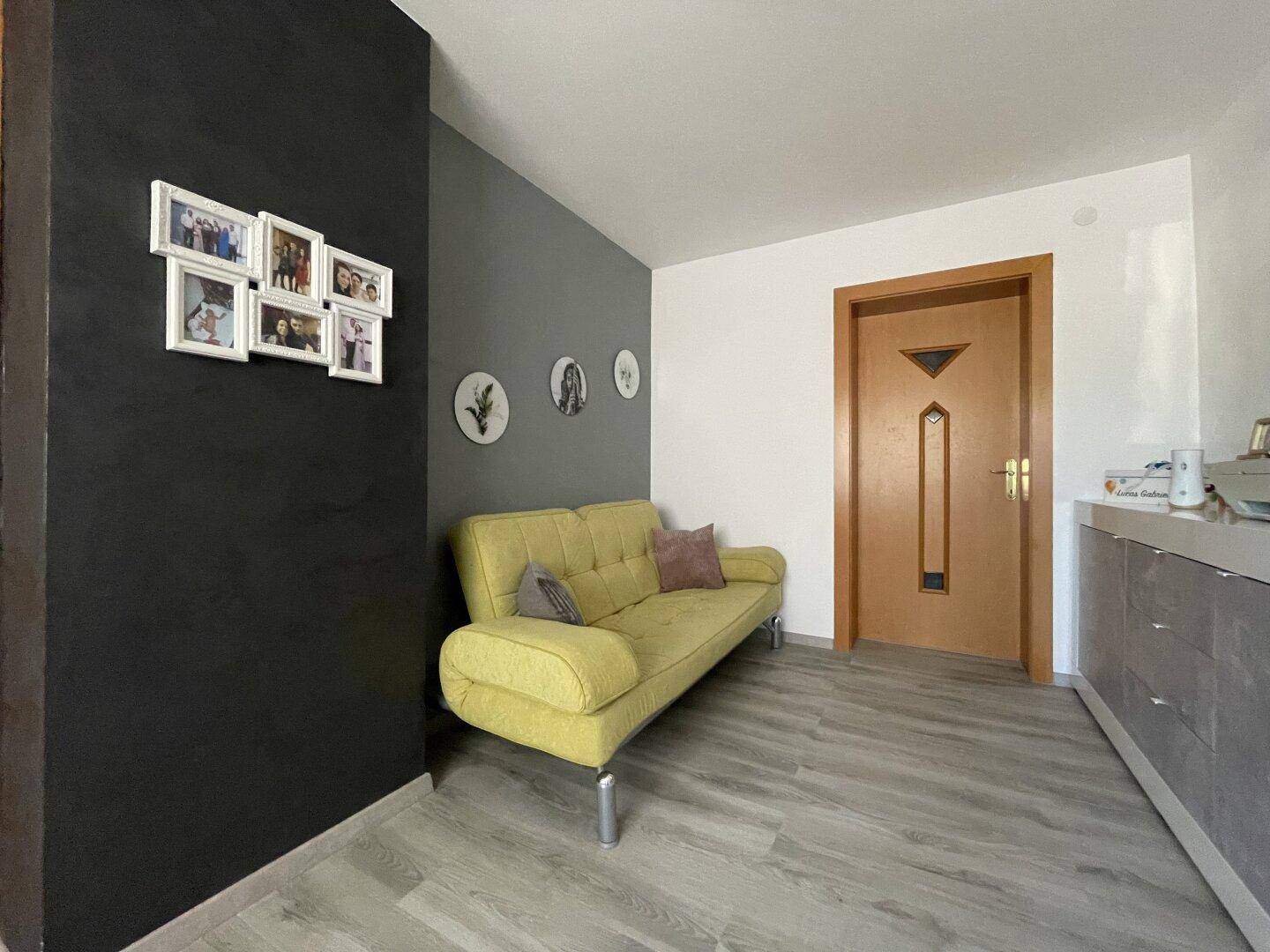 Gemütlicher Bereich mit gelbem Sofa, Laminatboden und dekorativer Wandgestaltung.