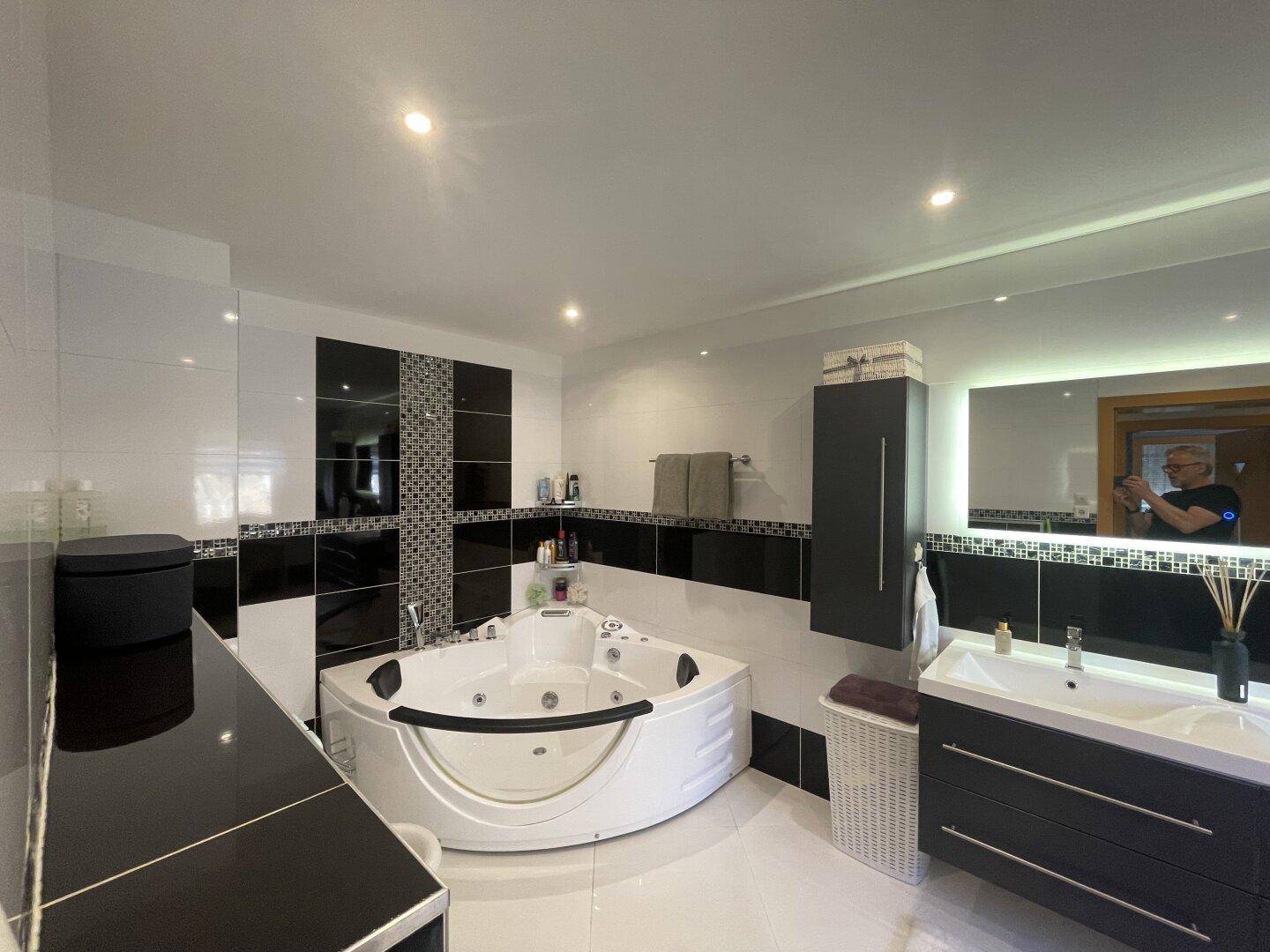 Elegantes Badezimmer mit Whirlpool-Badewanne, Doppelwaschbecken und stilvollen schwarzen Fliesen.