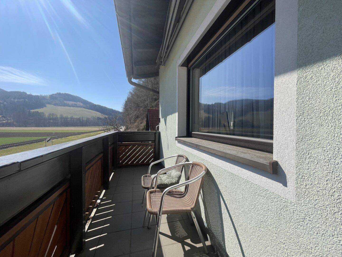 Sonniger Balkon mit Sitzgelegenheiten und weitem Blick auf die grüne Landschaft.