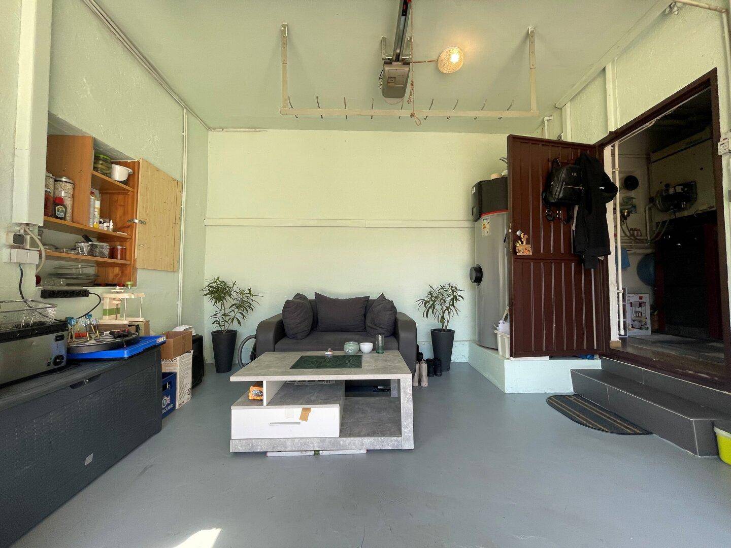 Umfunktionierte Garage mit Sitzbereich, Regalen und direktem Zugang nach draußen.