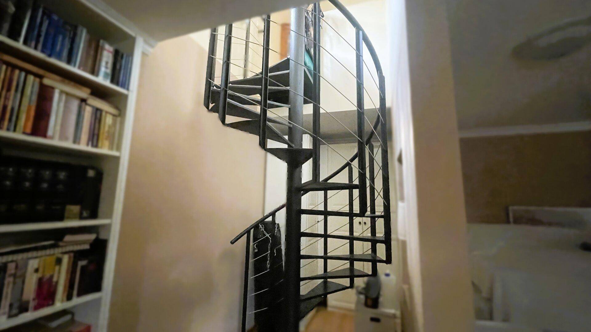 Elegante schwarze Wendeltreppe mit Metallgeländer, umgeben von Bücherregalen.