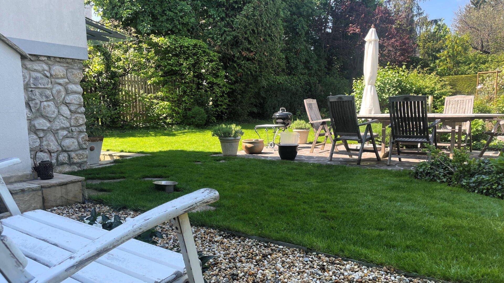 Sonniger Gartenbereich mit Rasen, Kies und einer möblierten Terrasse für entspannte Stunden.