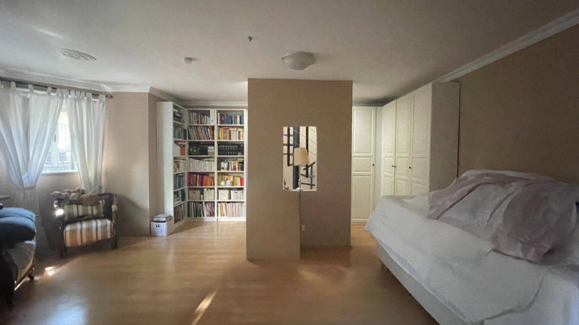 Geräumiges Schlafzimmer mit Holzboden, Einbauschränken und einem großen Bücherregal.