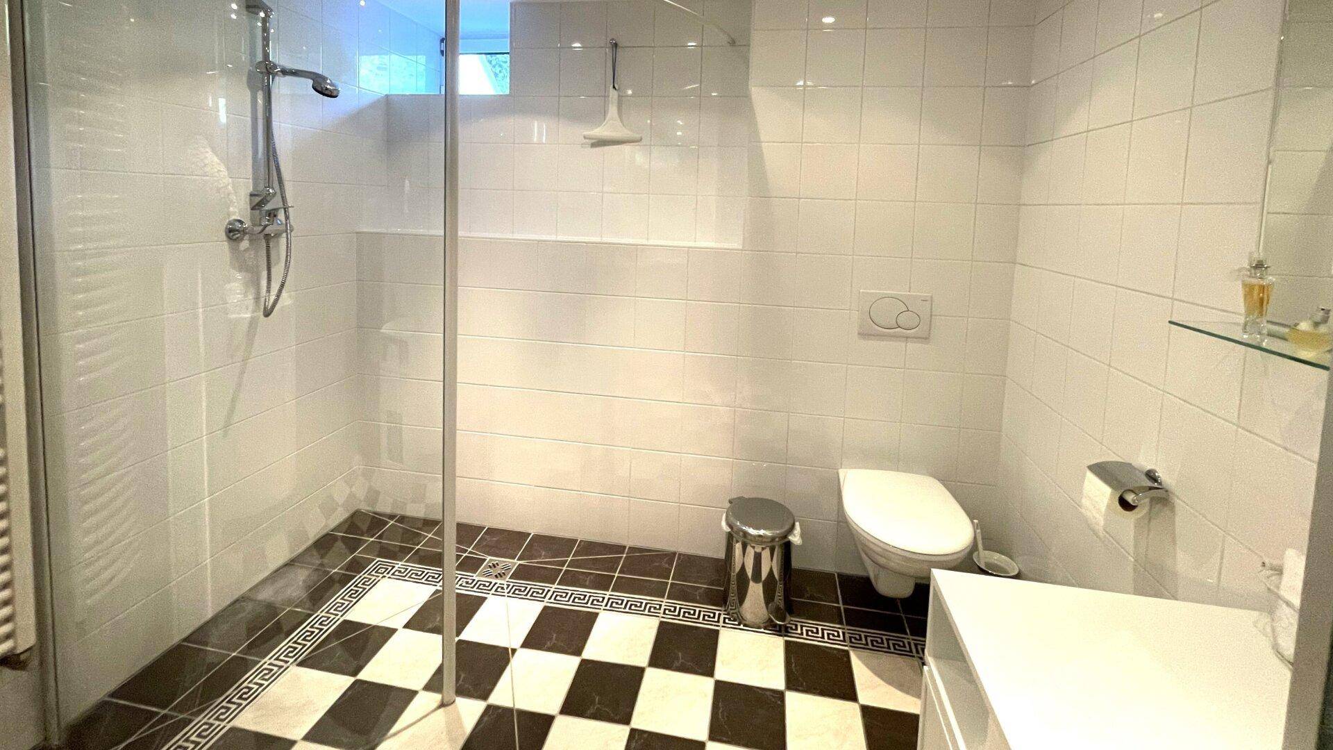 Modernes Badezimmer mit großer begehbarer Dusche, Wand-WC und Schachbrettmuster-Fliesen.