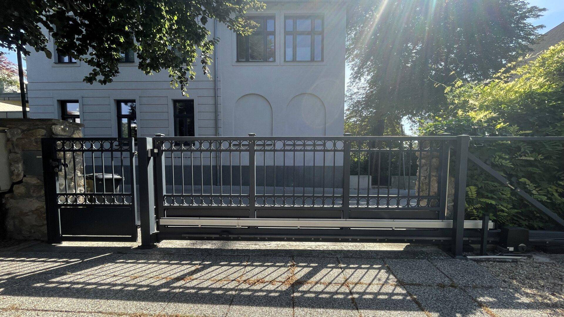 Modernes Einfahrtstor aus Metall vor einem Gebäude mit klassischer Architektur.