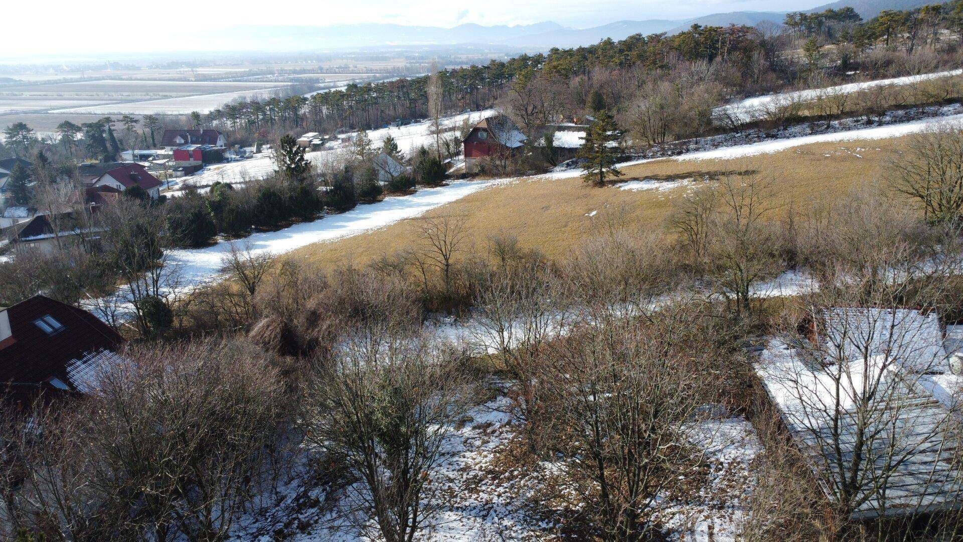 Weitläufige Luftaufnahme einer verschneiten Hügellandschaft mit Häusern und Fernblick.