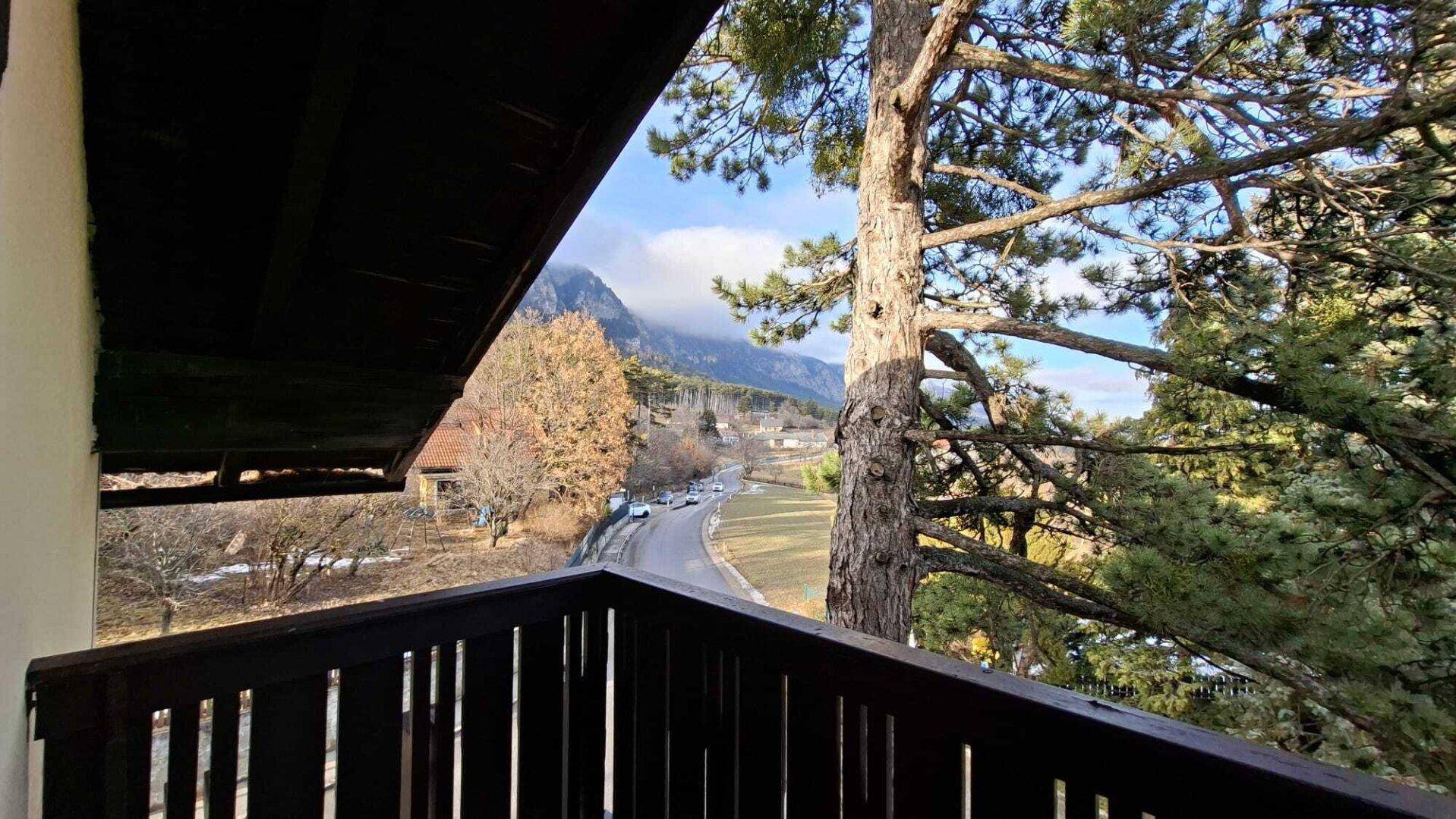 Blick vom Balkon auf die Straße, Bäume und die umliegende Berglandschaft.
