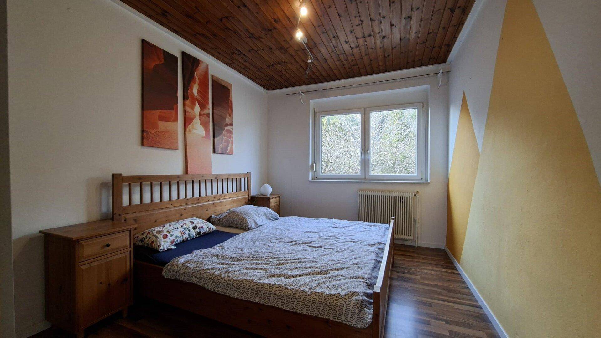 Schlafzimmer mit Doppelbett, Holzdecke, Holzfußboden und farbiger Wandgestaltung.