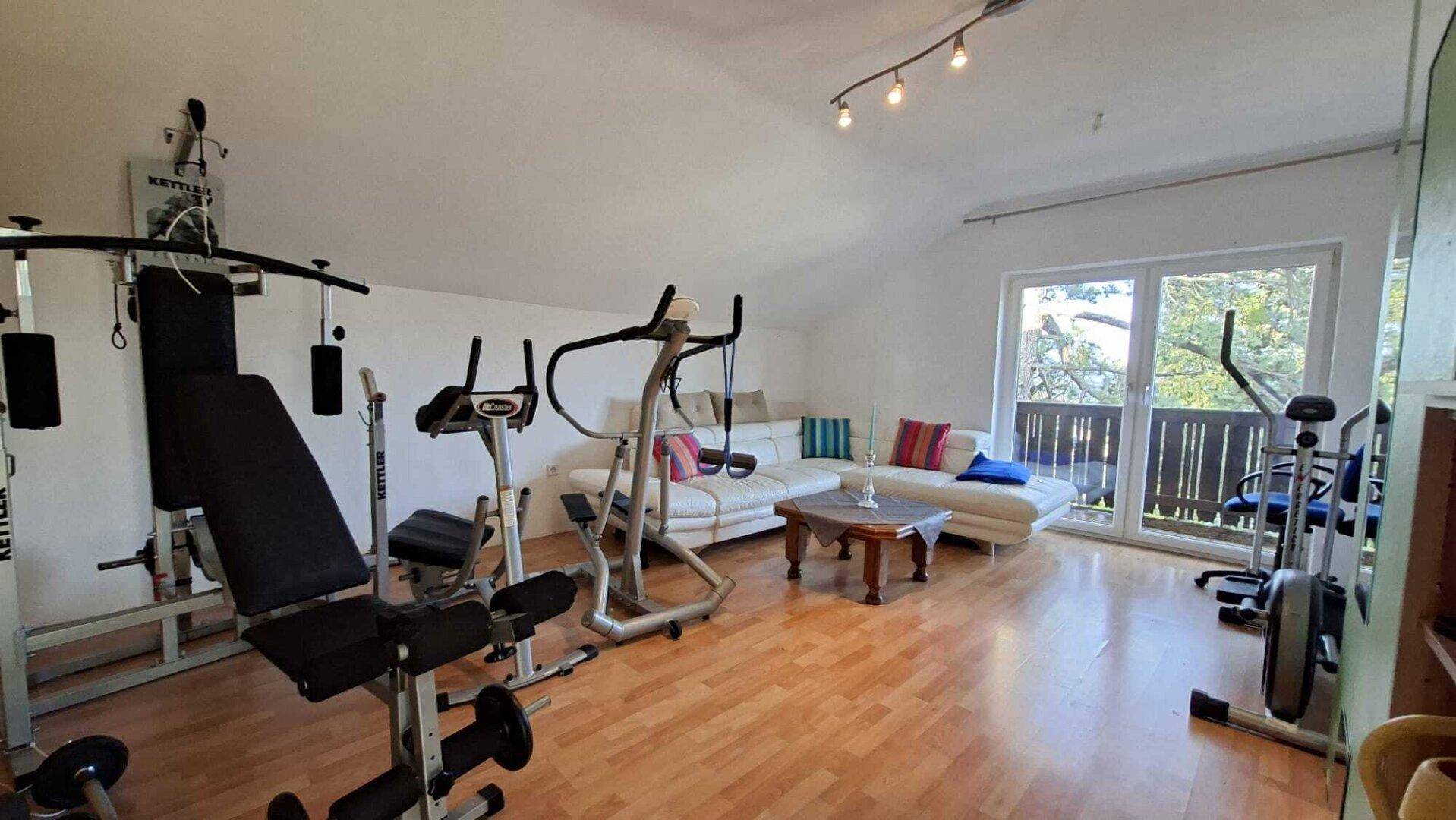 Geräumiger Raum mit Fitnessgeräten, Sofa und Zugang zu einem Balkon.