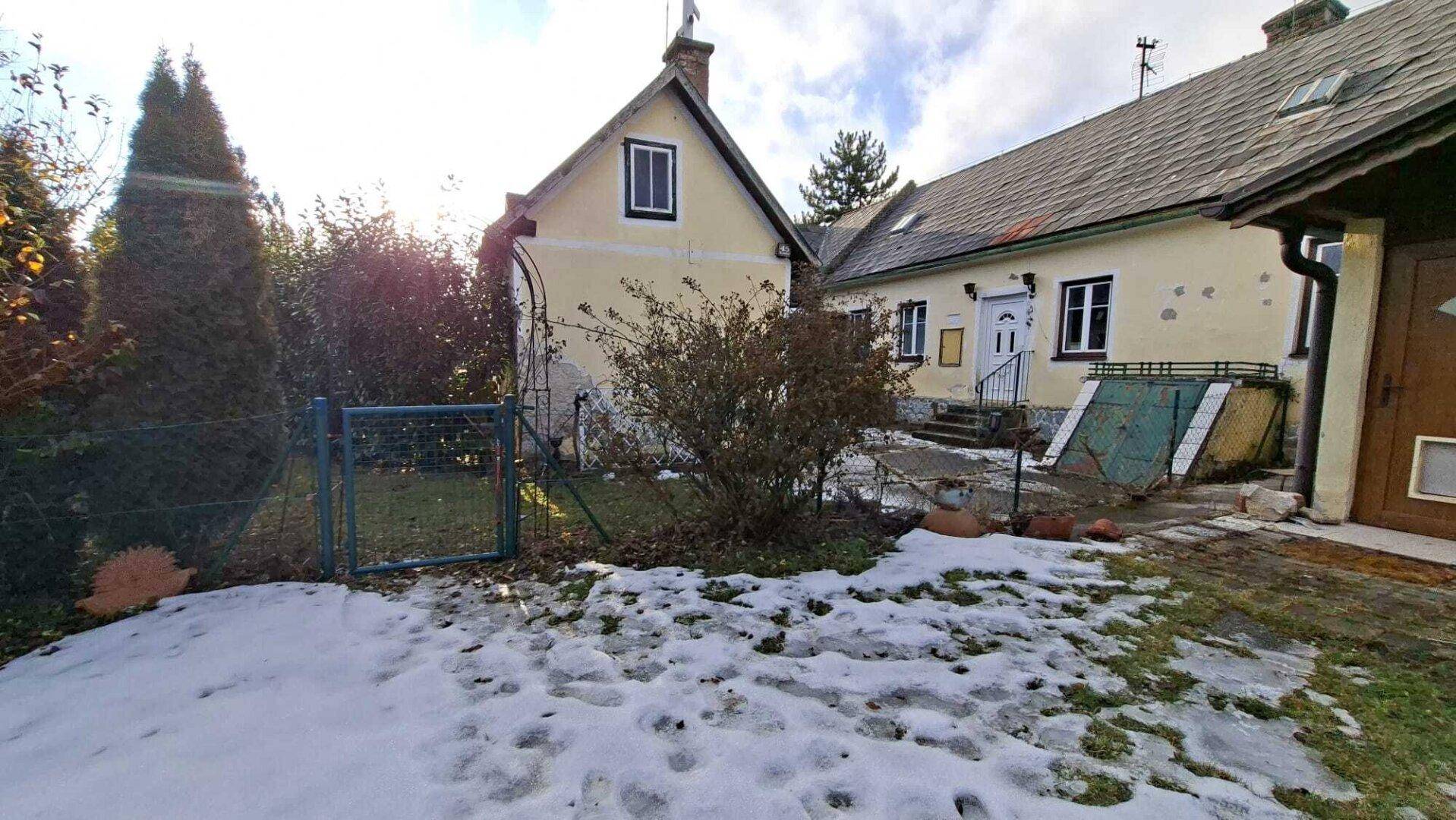 Gartenbereich vor dem Haus mit Schnee, Zaun und Büschen im Sonnenlicht.