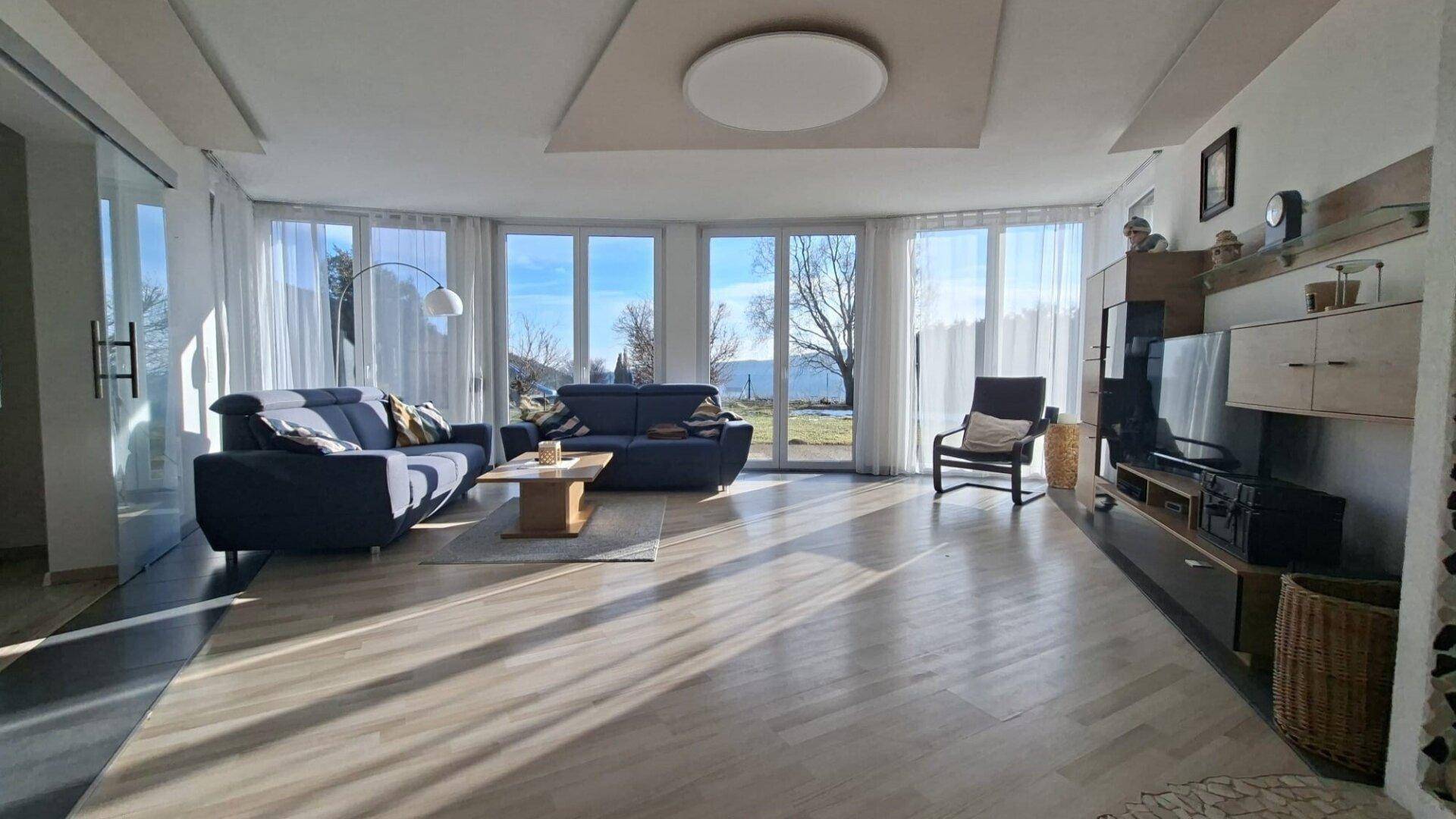 Geräumiges Wohnzimmer mit viel Tageslicht, Holzboden und moderner Einrichtung, sehr hell.