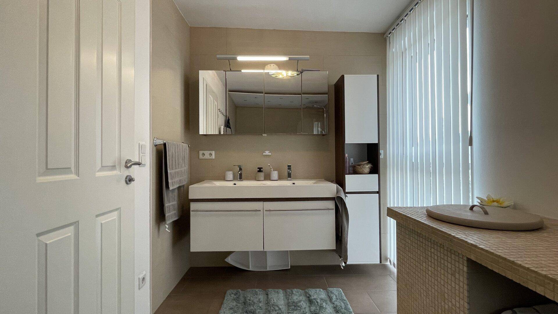 Modernes Badezimmer mit Doppelwaschbecken, Spiegelschrank und großen Fliesen.