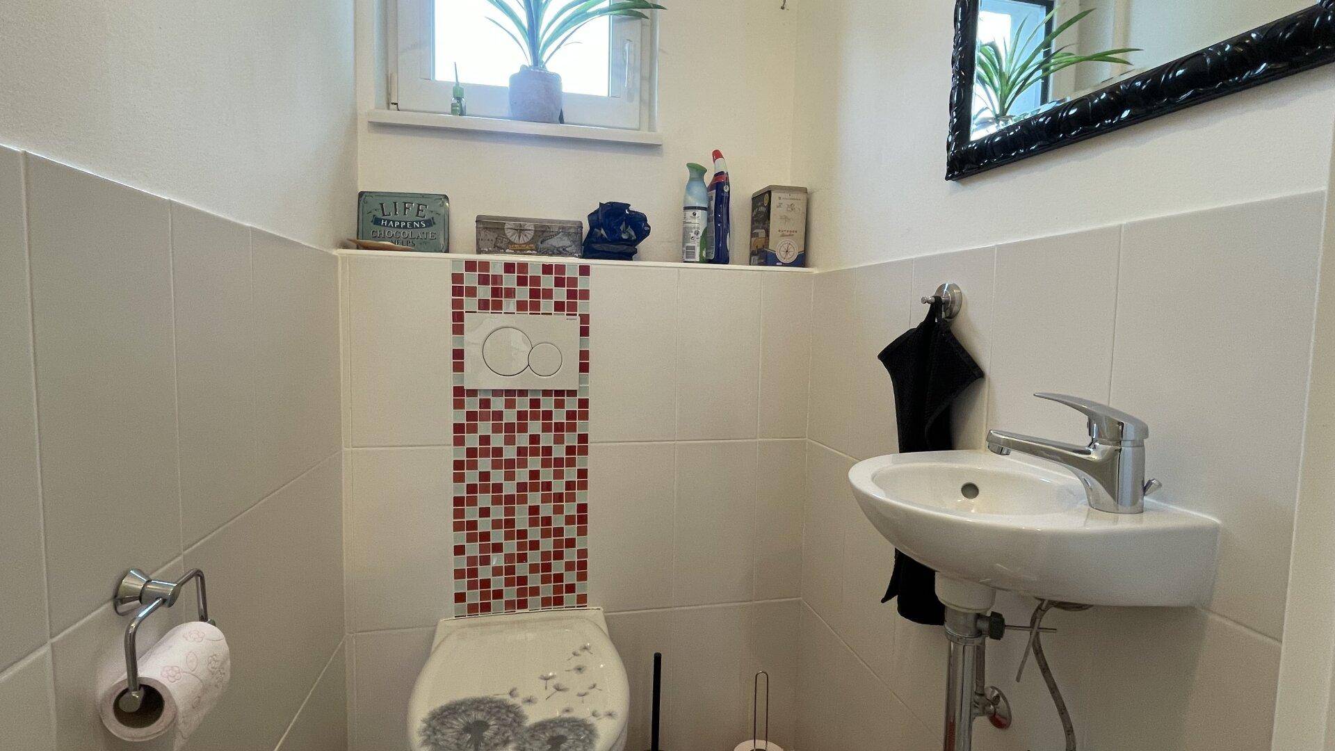 Kleines Gäste-WC mit weiß-roten Fliesen, Wand-WC und kleinem Waschbecken.