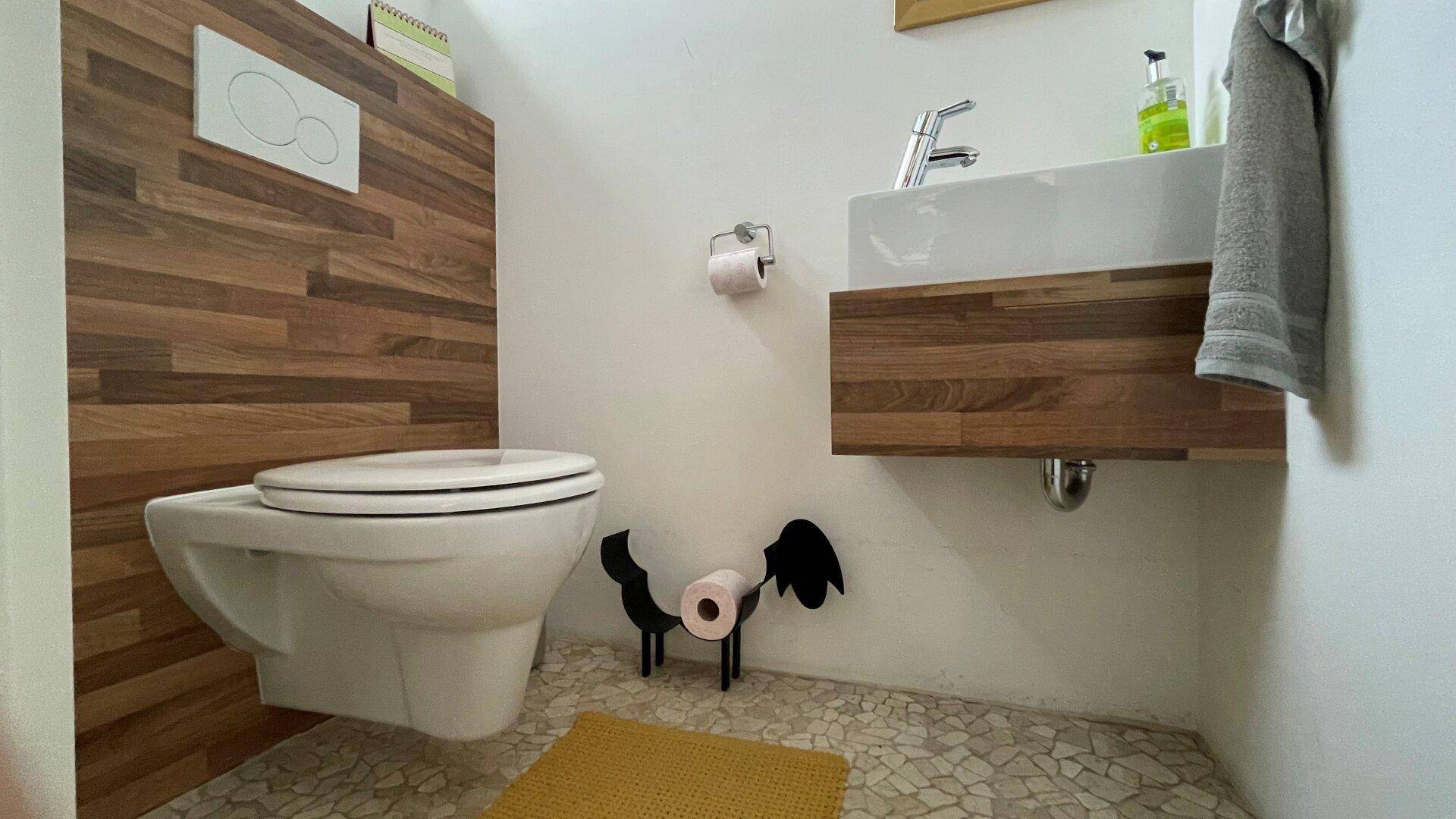 Modernes Gäste-WC mit Wand-WC, Waschbecken und Holzakzenten an der Wand.