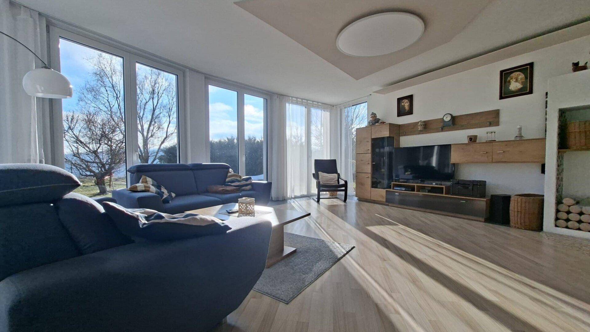 Helles Wohnzimmer mit großen Fensterfronten, Holzboden und bequemen Sofas, sonnendurchflutet.