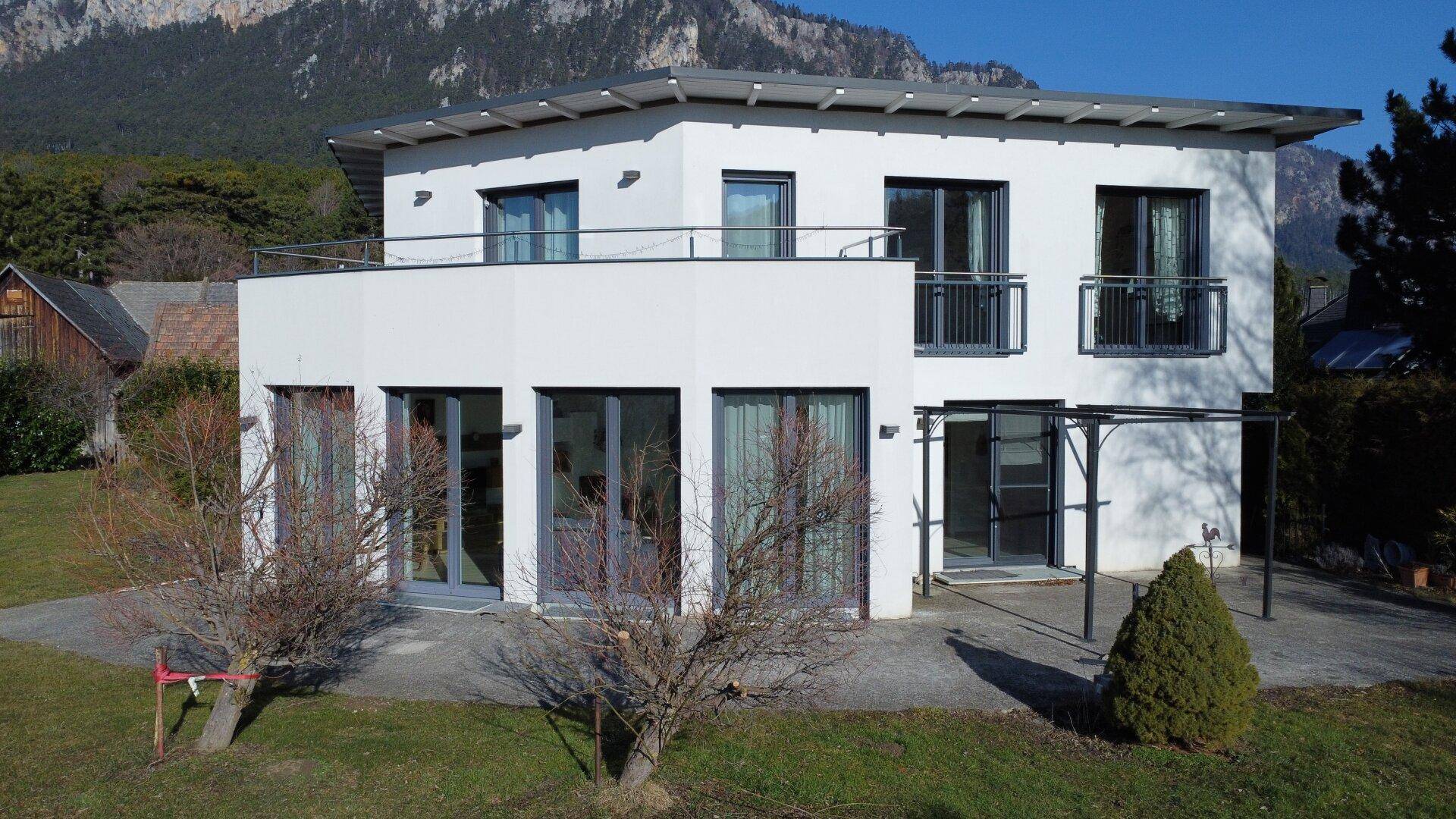 Weißes Einfamilienhaus mit großen Fenstern, Balkonen und einer Terrasse im Erdgeschoss.