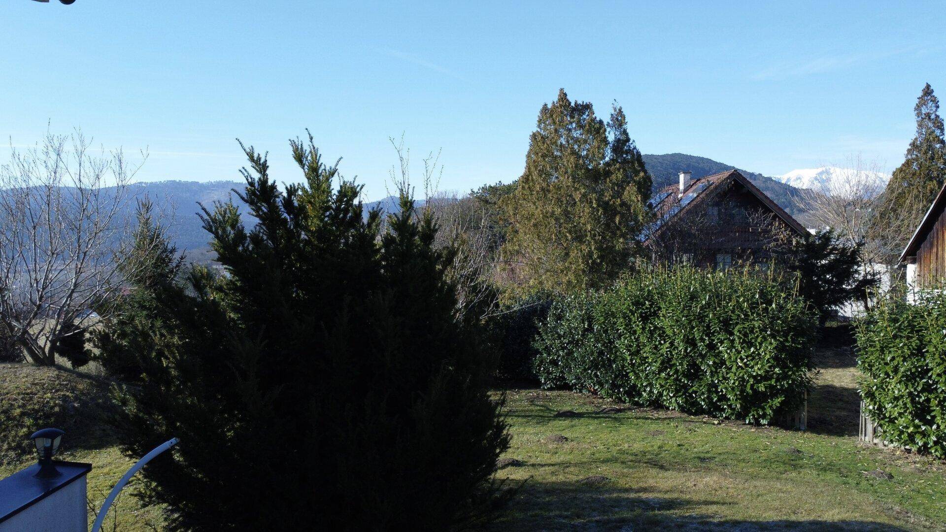 Panoramablick von der Immobilie auf die umliegende Natur mit Hecken, Bäumen und schneebedeckten Bergen.
