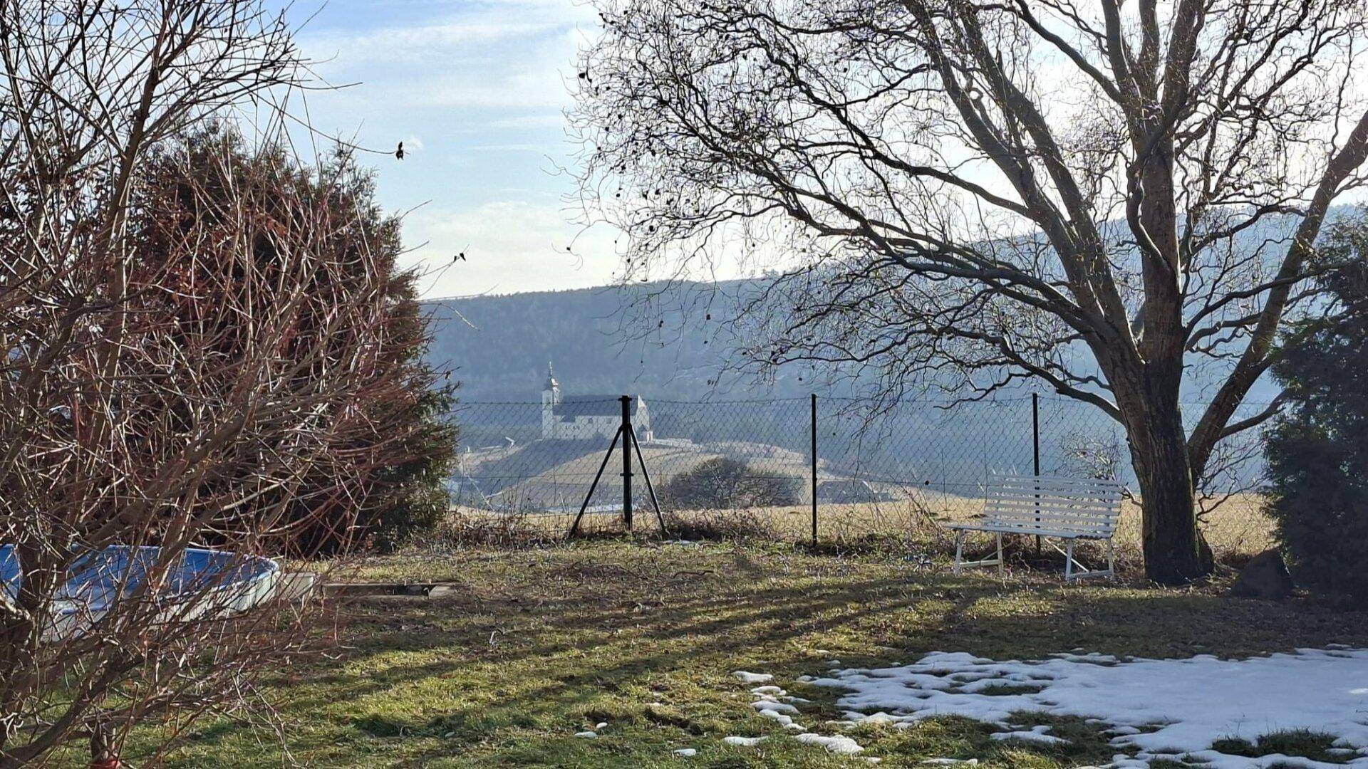 Gartenansicht mit Bäumen, Zaun und einem malerischen Blick auf eine Kirche in der Ferne.