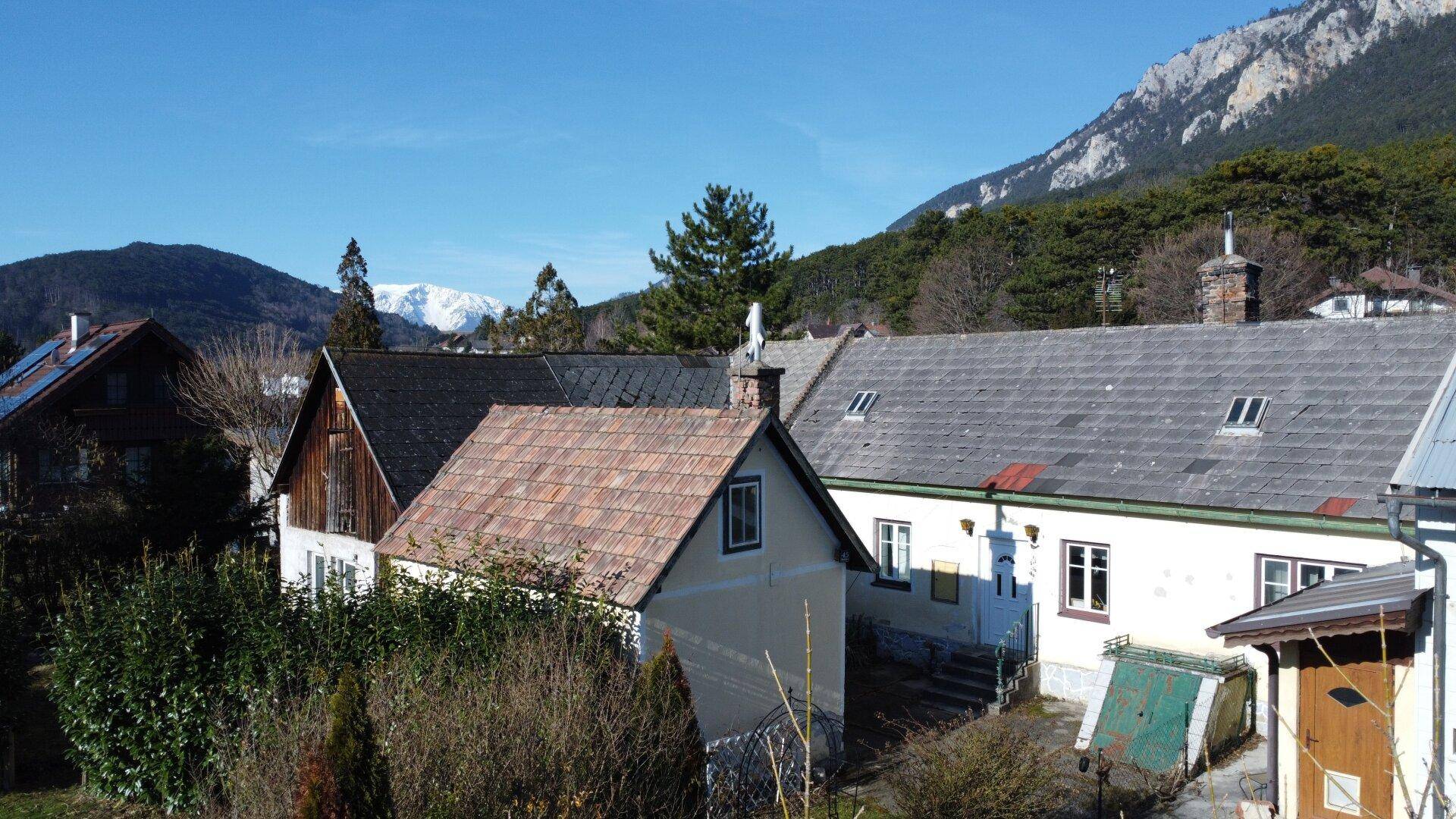 Mehrere Gebäude mit traditionellen Dächern und Bergblick unter blauem Himmel.