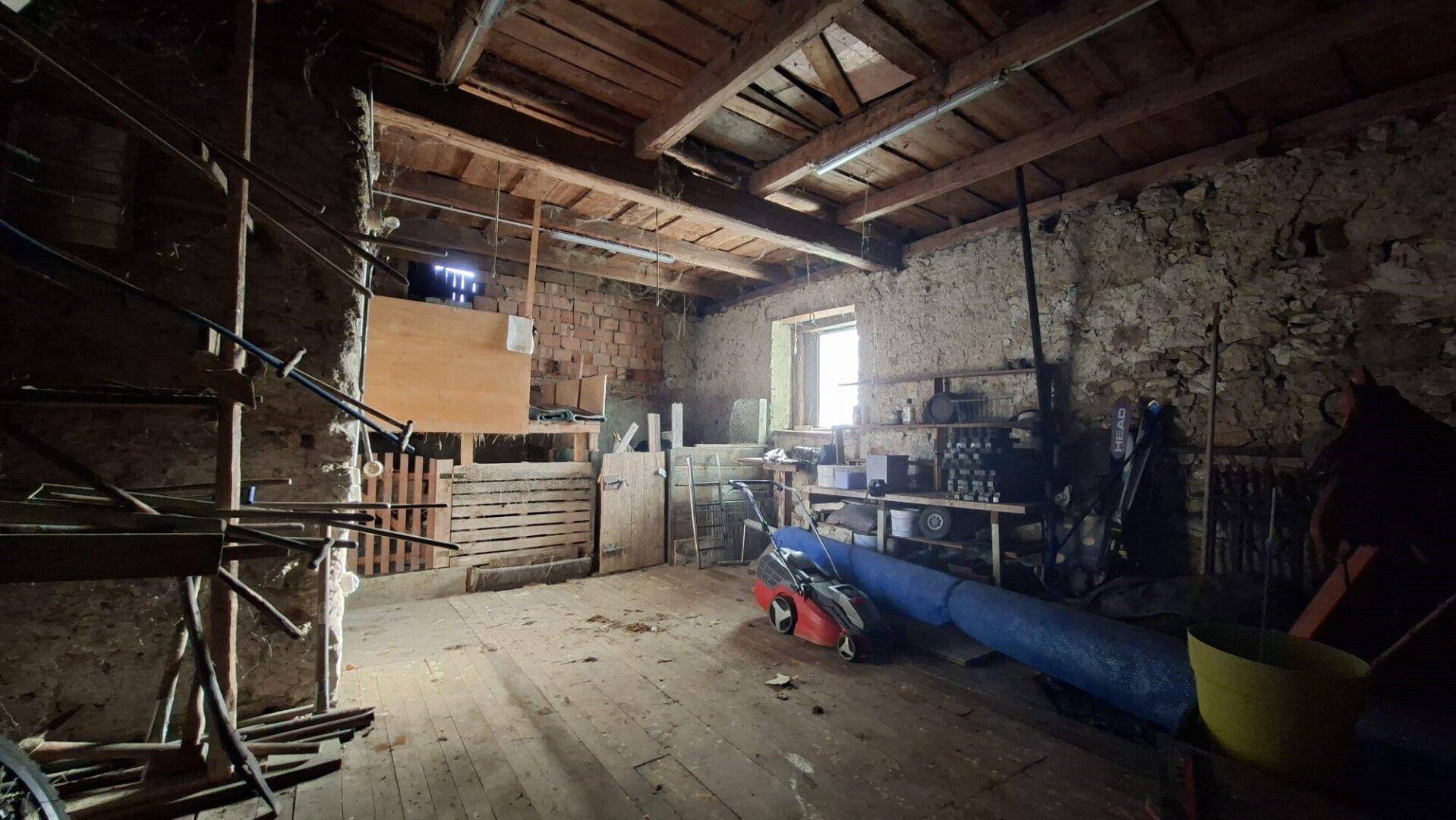 Großer, leerer Dachbodenraum mit sichtbaren Holzbalken, Steinwänden und Holzboden, der Renovierung benötigt.