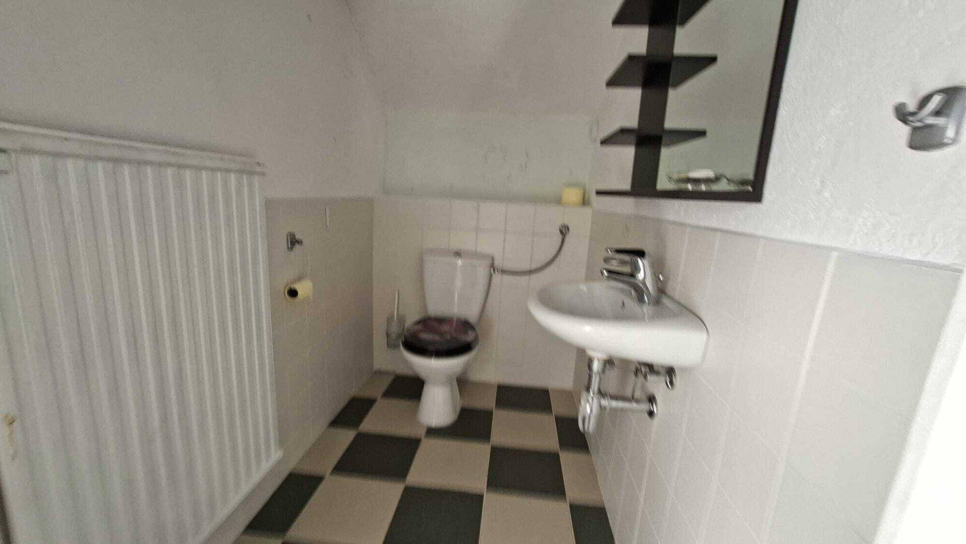 Kleines WC mit Toilette, Waschbecken und schwarz-weißem Fliesenboden.