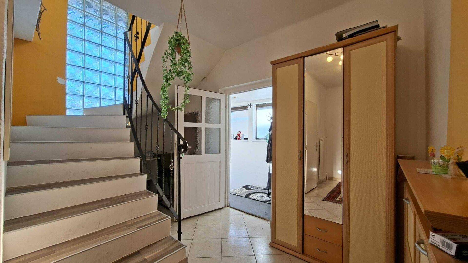 Eingangsbereich mit Treppe, Spiegelschrank und Fliesenboden.