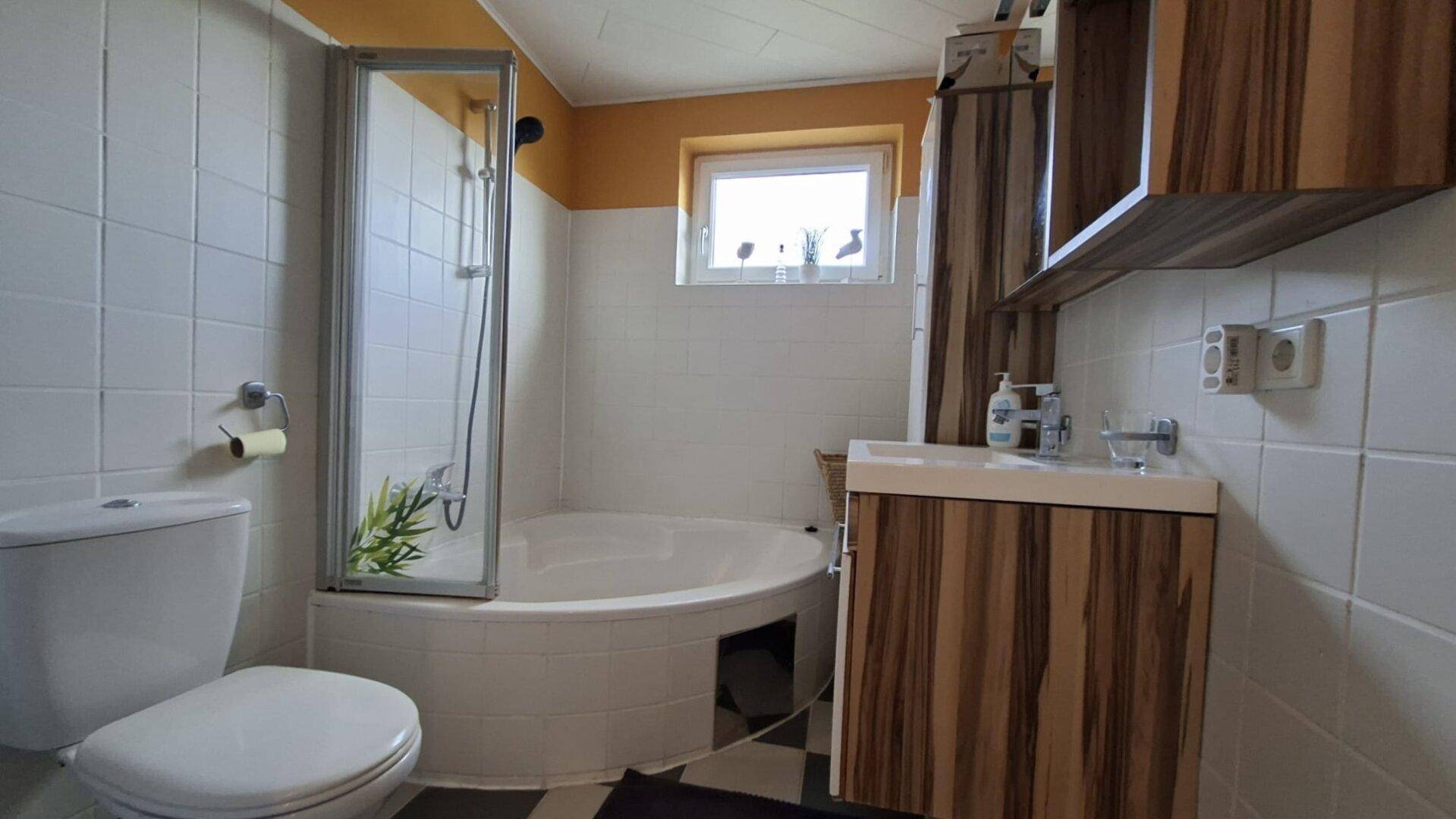 Badezimmer mit Dusche, Eckbadewanne, WC und Holzdekor-Waschtisch.