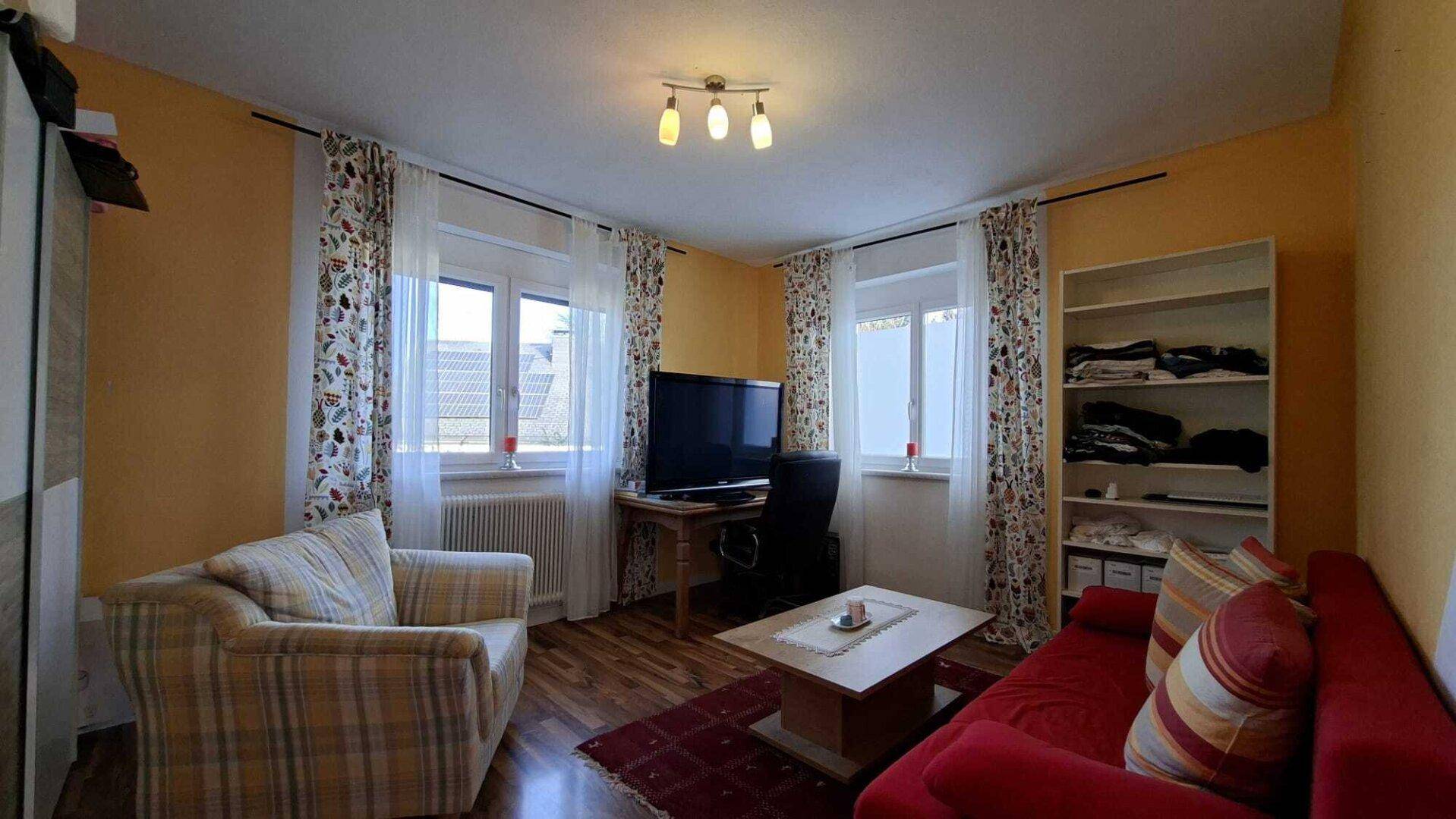 Gemütliches Wohnzimmer mit Sofa, Sessel, Fernseher und Holzfußboden.