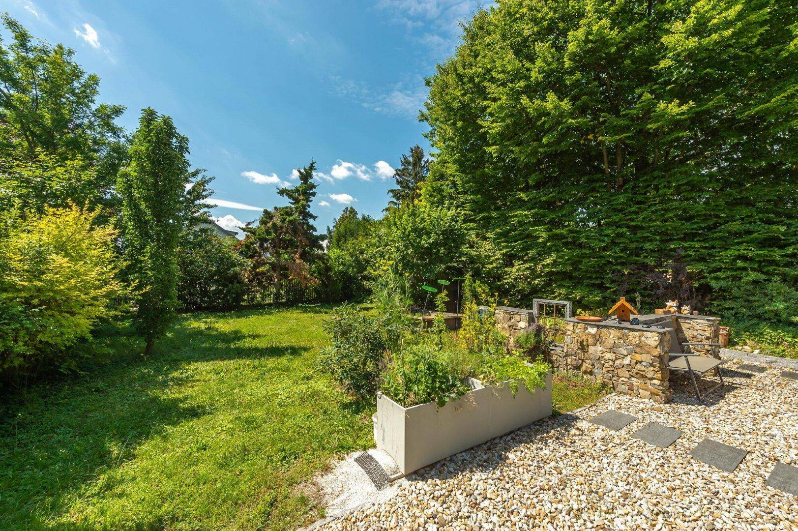 Großer, gepflegter Garten mit Rasenfläche, Hochbeet und altem Baumbestand.