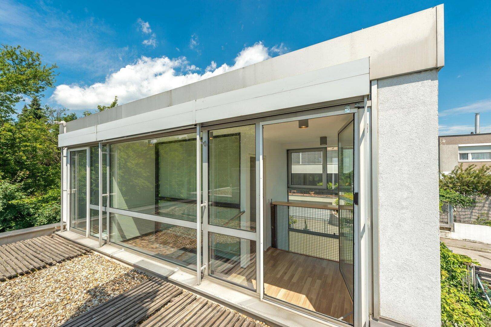 Dachterrasse mit Holzboden und großen Glasfronten, die viel Licht ins Innere lassen.