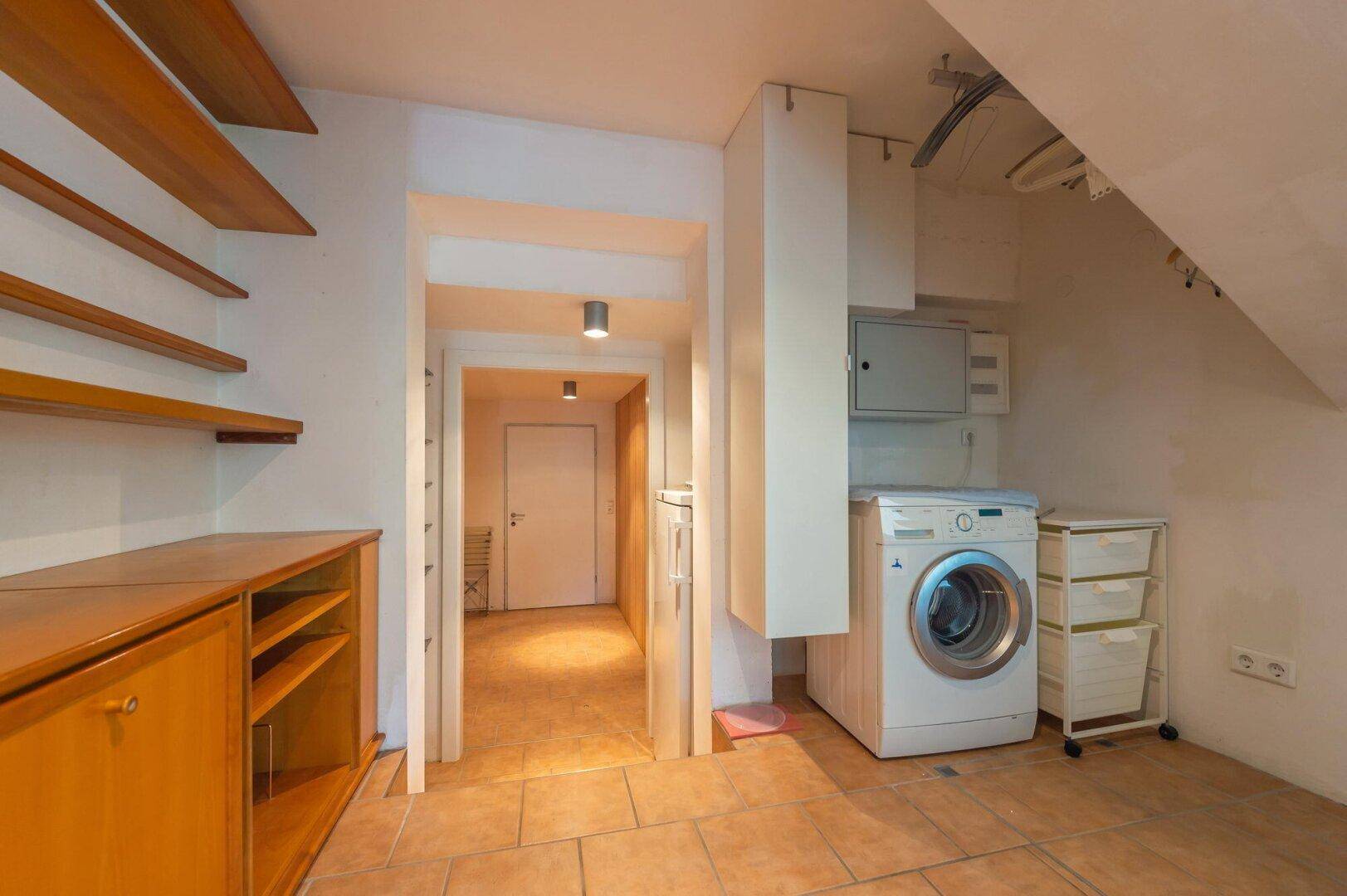 Praktischer Hauswirtschaftsraum mit Waschmaschine und Stauraum unter der Treppe.