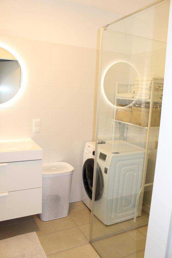 Helles Badezimmer mit Duschkabine, Waschmaschine und modernem Waschtisch, effizient genutzt.