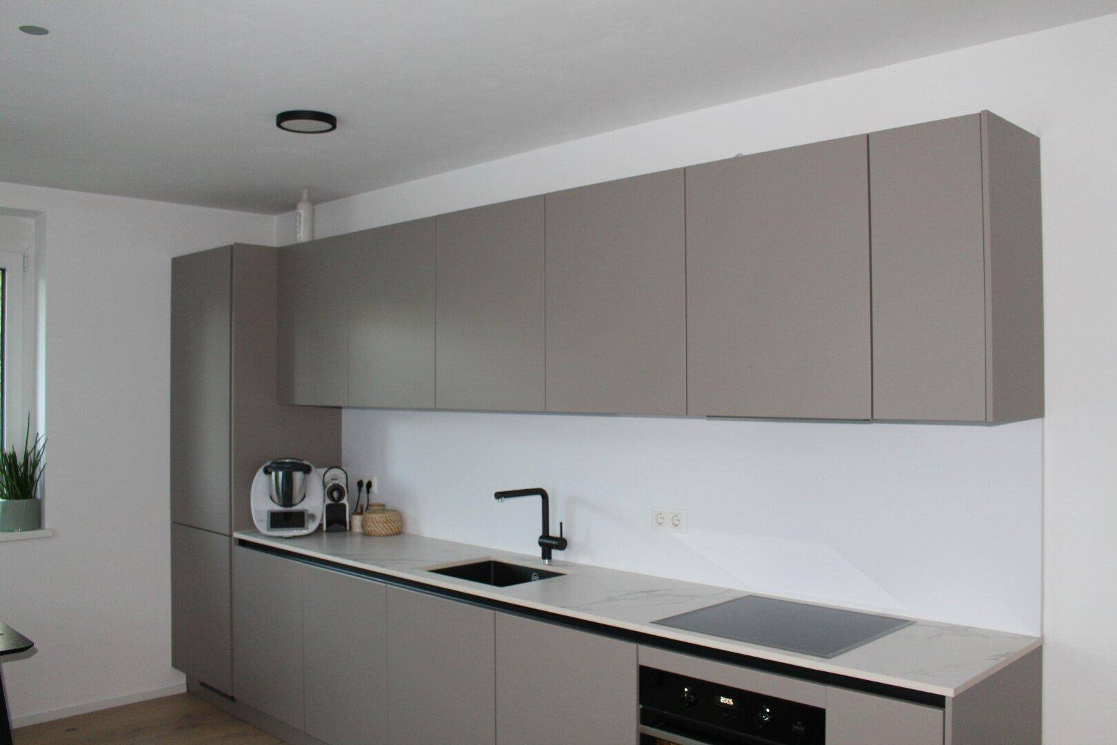 Moderne Küche mit grauen Schränken, Induktionskochfeld und weißer Arbeitsplatte, funktional und stilvoll.