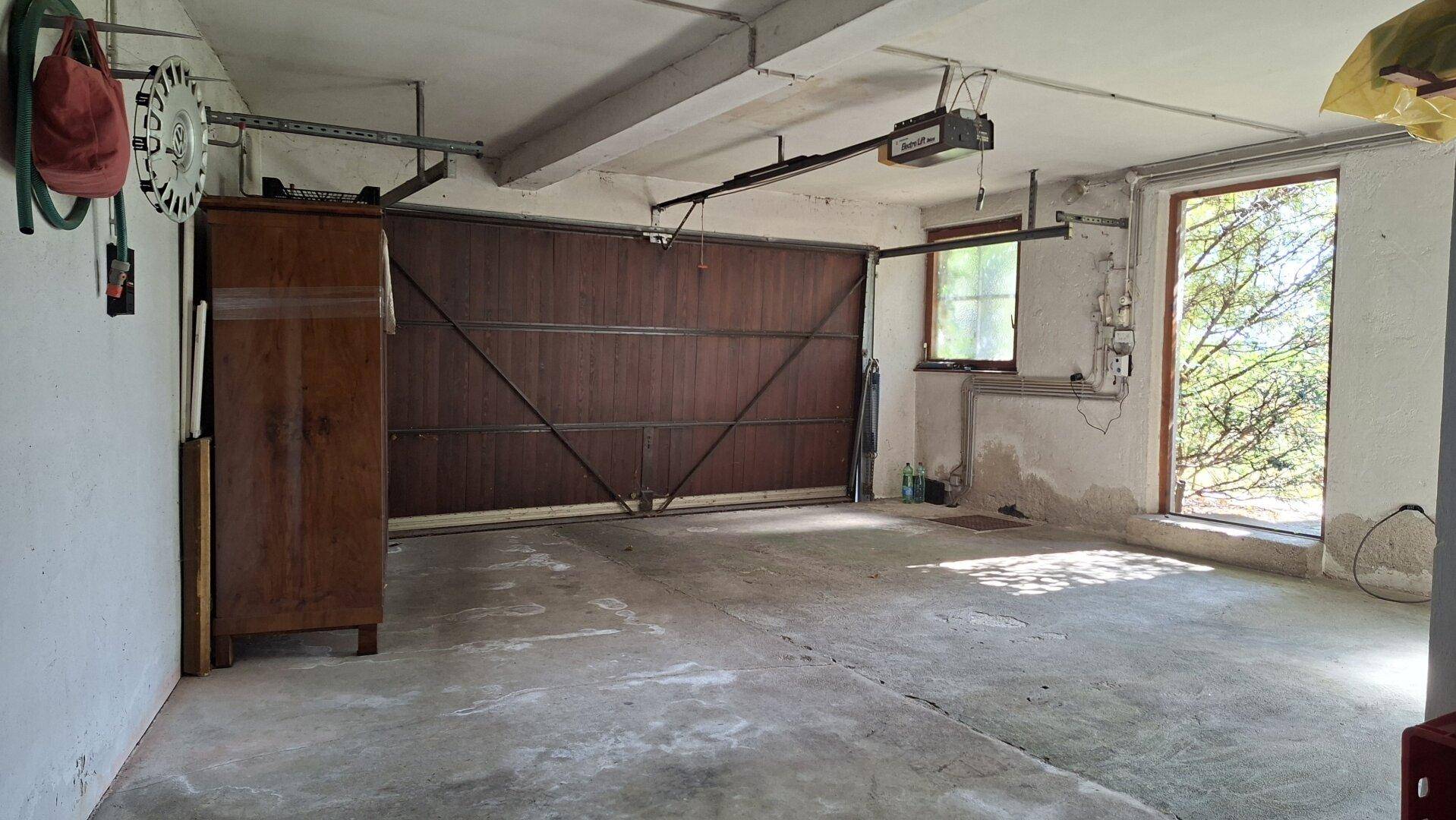 Geräumige Garage mit großem Holztor, Betonboden und Fenstern für Tageslicht.