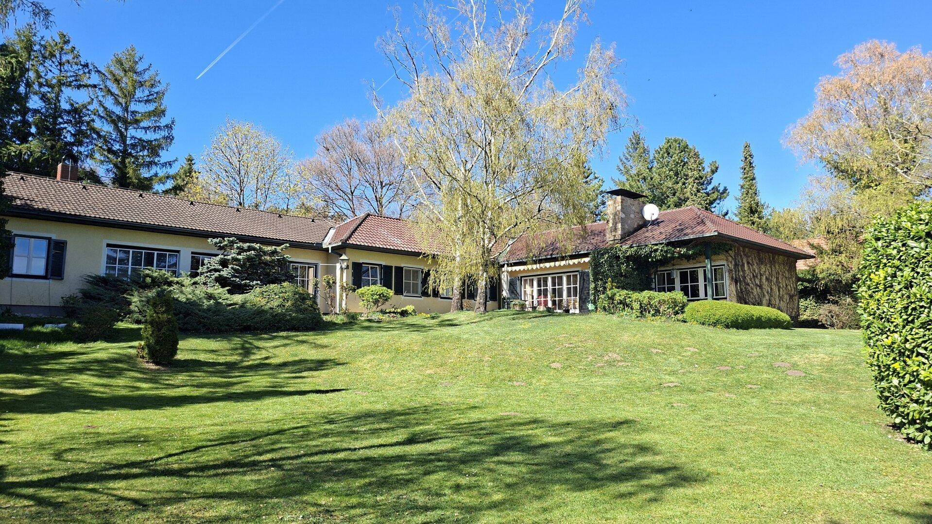 Ansicht des Hauses vom weitläufigen Garten aus mit gepflegtem Rasen und altem Baumbestand.