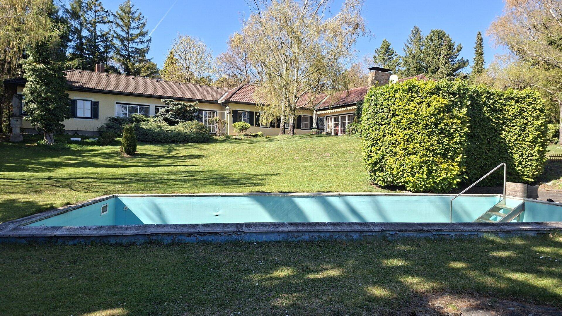 Großer Außenpool im weitläufigen Garten mit Blick auf das charmante Landhaus.
