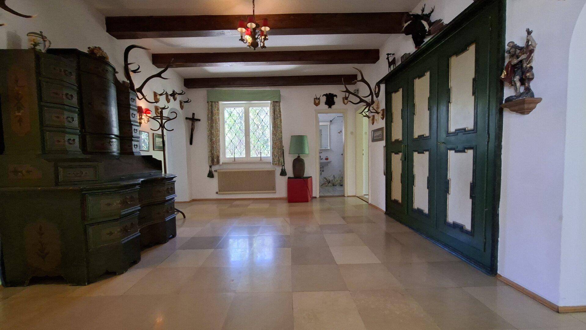 Geräumiger Eingangsbereich mit Fliesenboden, Holzbalken und traditioneller Hirschgeweih-Dekoration.