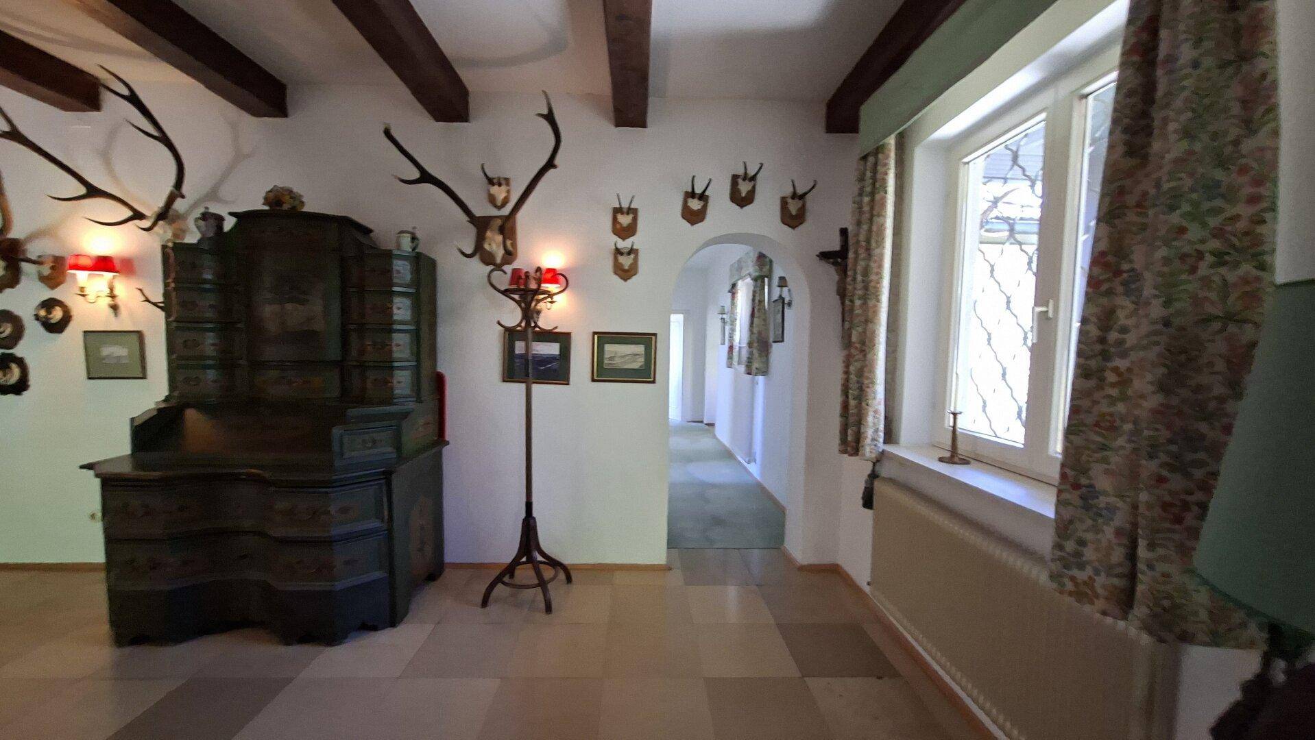 Heller Flur mit Fliesenboden, Holzbalken und traditionellen Jagdtrophäen an den Wänden.