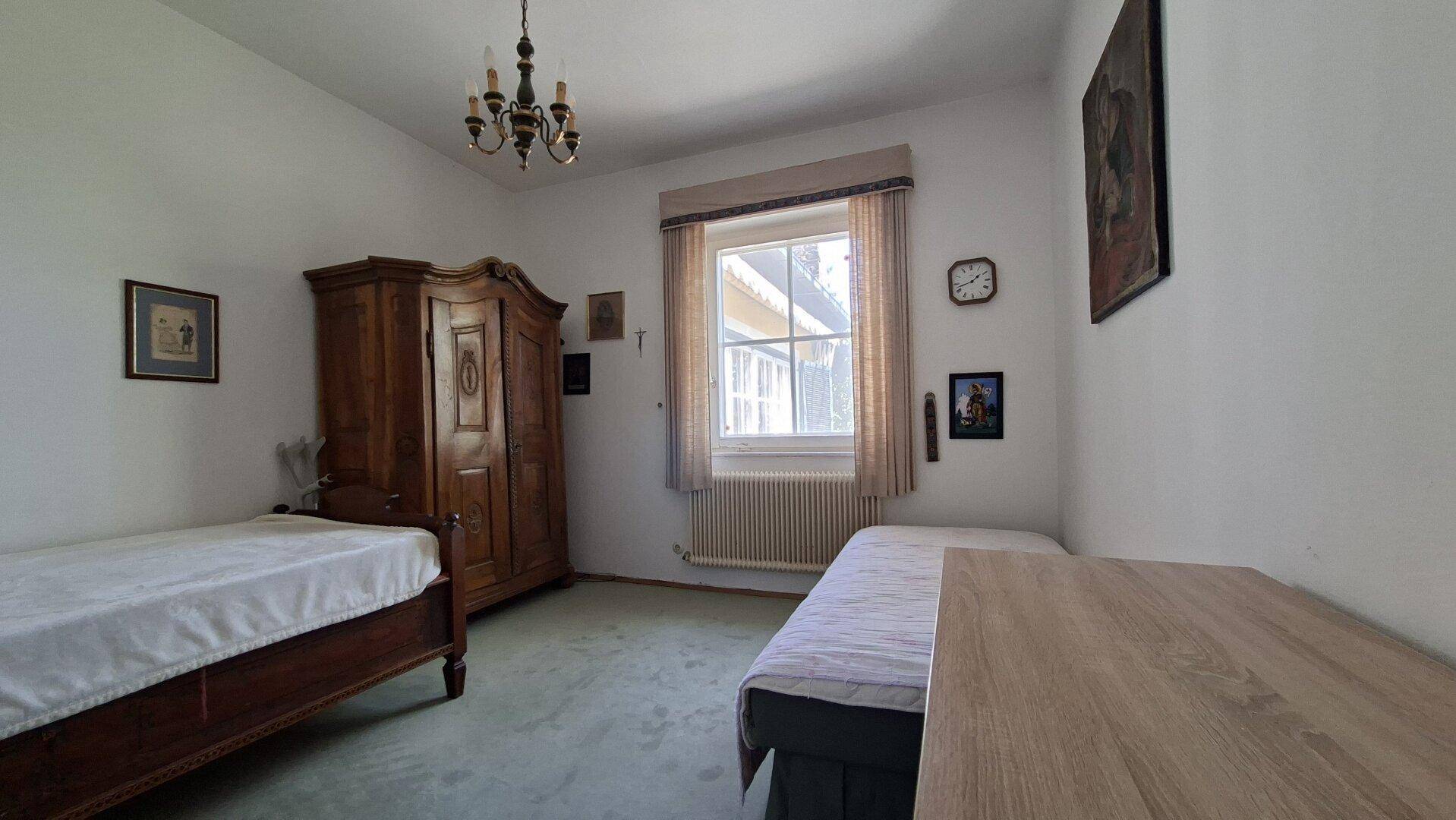 Schlafzimmer mit zwei Einzelbetten, klassischem Holzschrank und grünem Teppichboden.