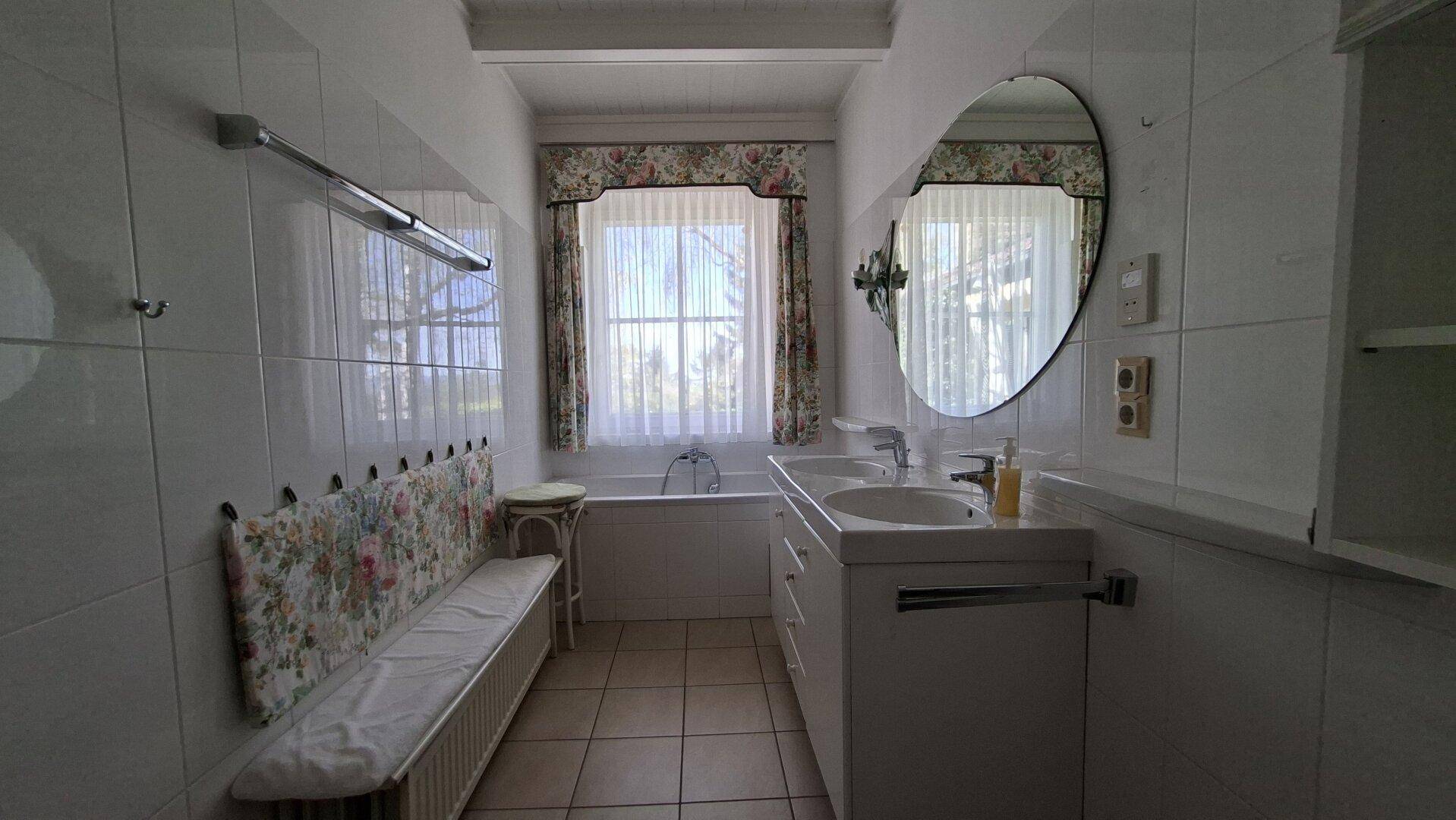Helles Badezimmer mit Doppelwaschbecken, Badewanne und Fenster, gut beleuchtet.