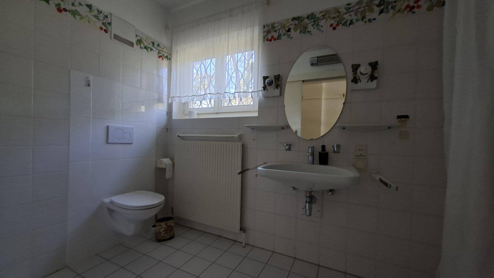 Kleines Badezimmer mit WC, Waschbecken und Fenster, in hellem Design gehalten.