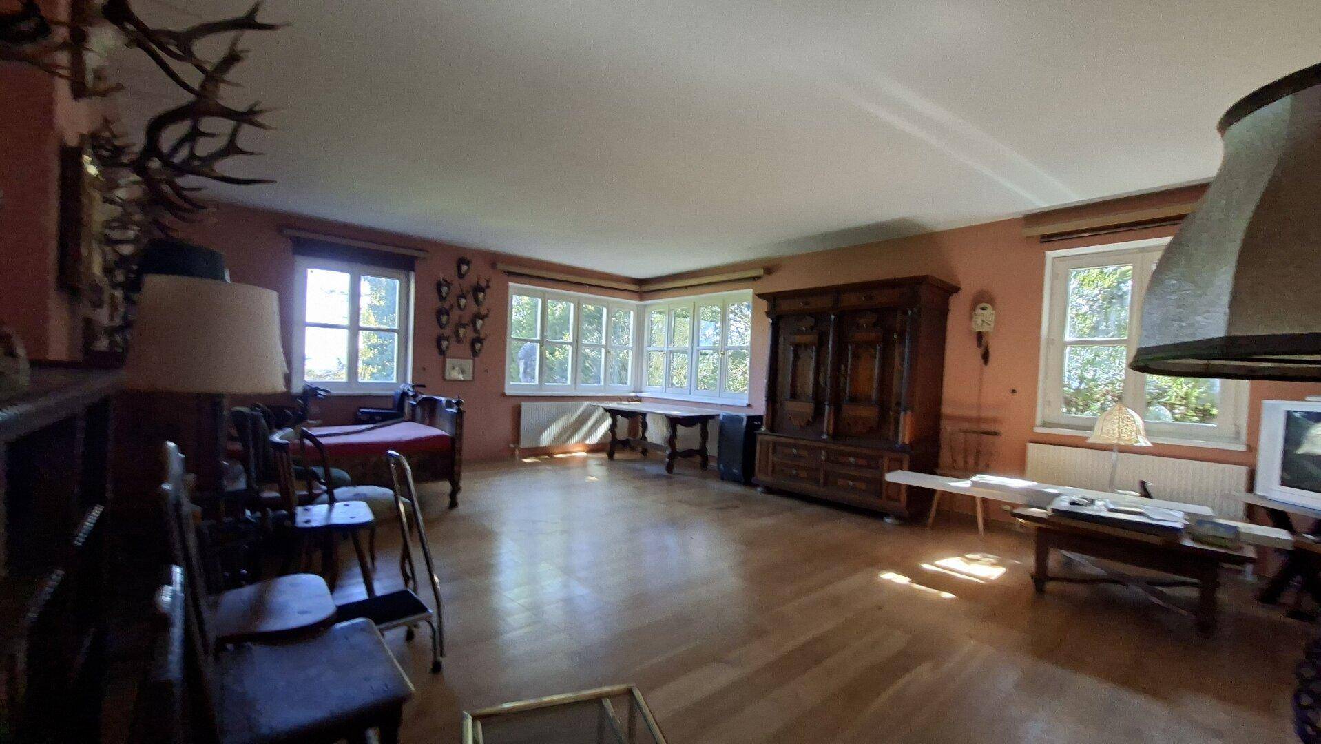 Geräumiges Wohnzimmer mit Holzboden, vielen Fenstern und traditionellen Möbeln.