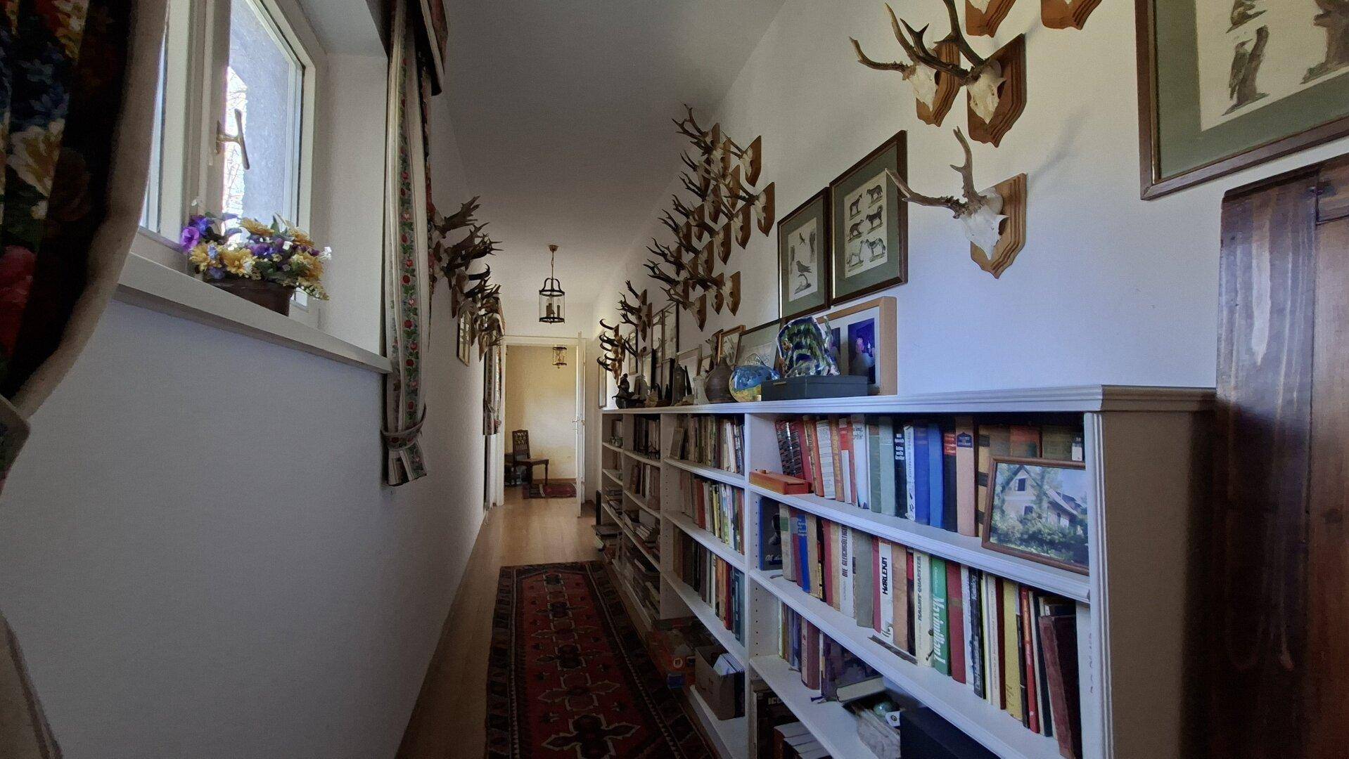 Langer Flur mit Bücherregalen, Holzboden und traditionellen Hirschgeweih-Dekorationen.