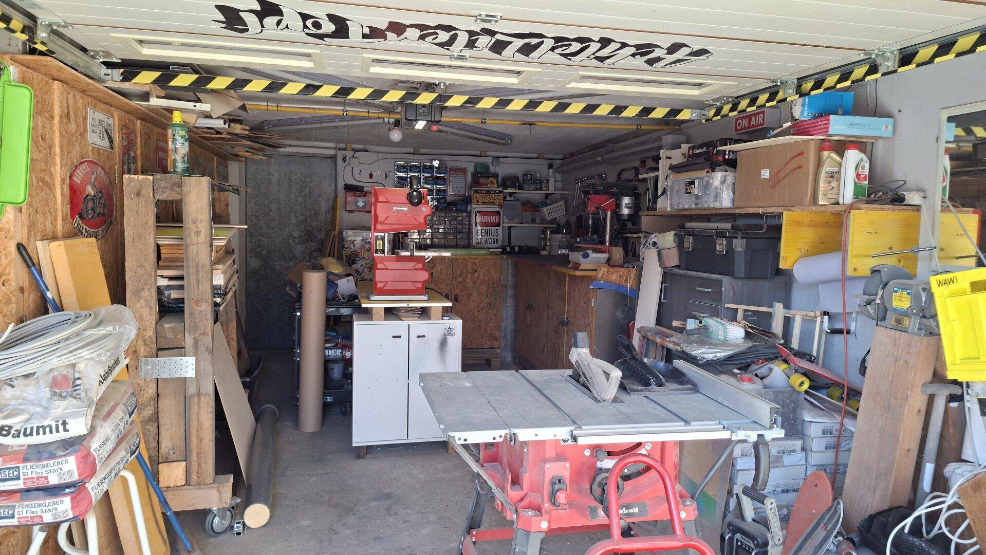 Geräumige Garage, die als Werkstatt genutzt wird, mit Werkzeugen, Maschinen und Lagerflächen.