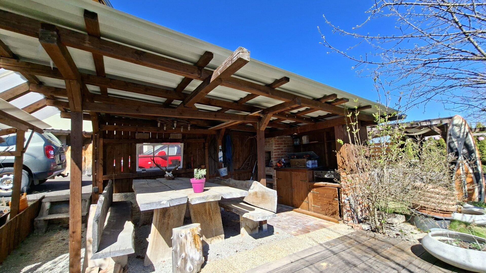 Überdachte Terrasse mit rustikalen Holzmöbeln und Grillbereich.