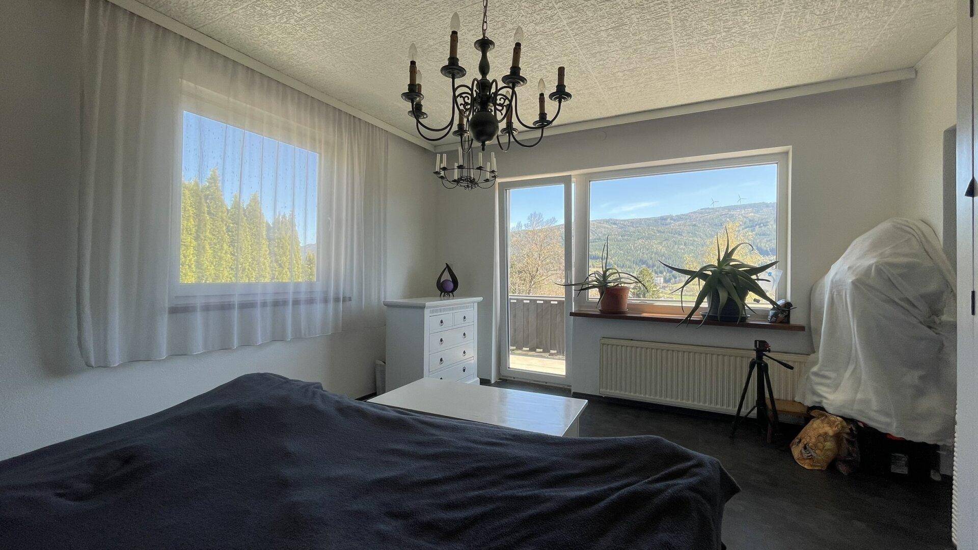 Helles Schlafzimmer mit Balkonzugang, weißer Kommode und Blick ins Grüne.