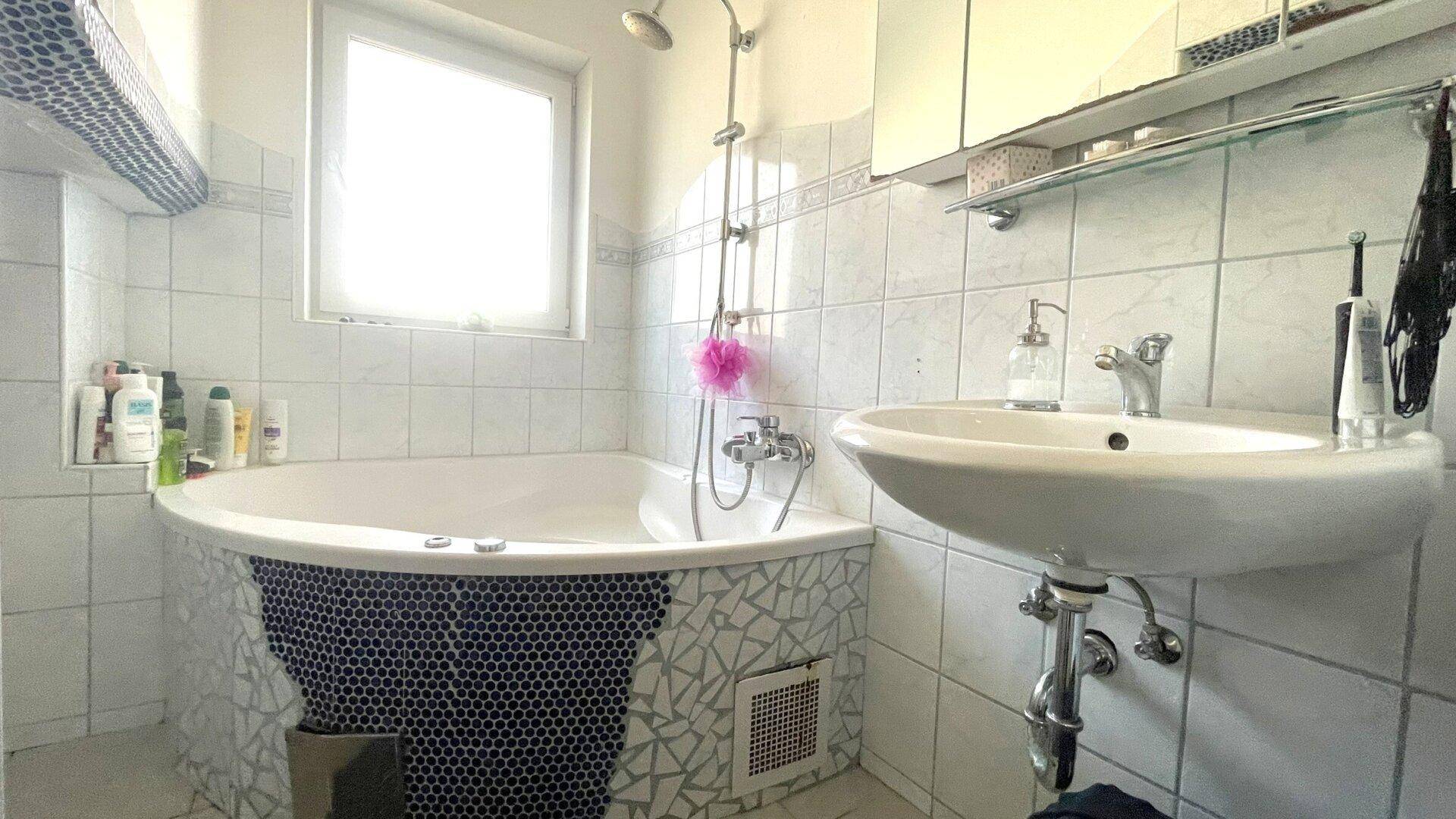 Badezimmer mit Badewanne, Waschbecken und weißen Fliesen.