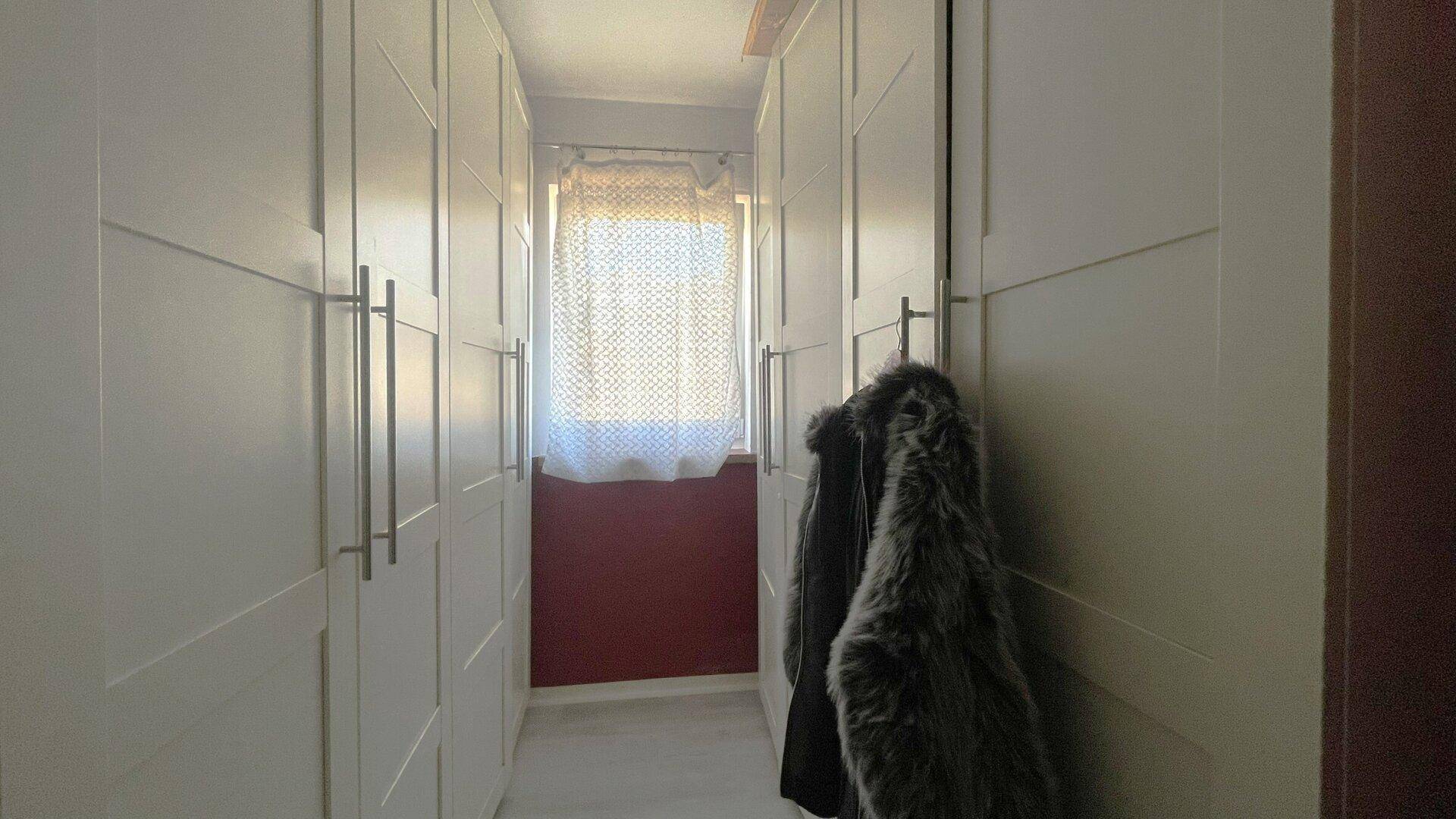 Flur mit beidseitigen Einbauschränken und Fenster am Ende.